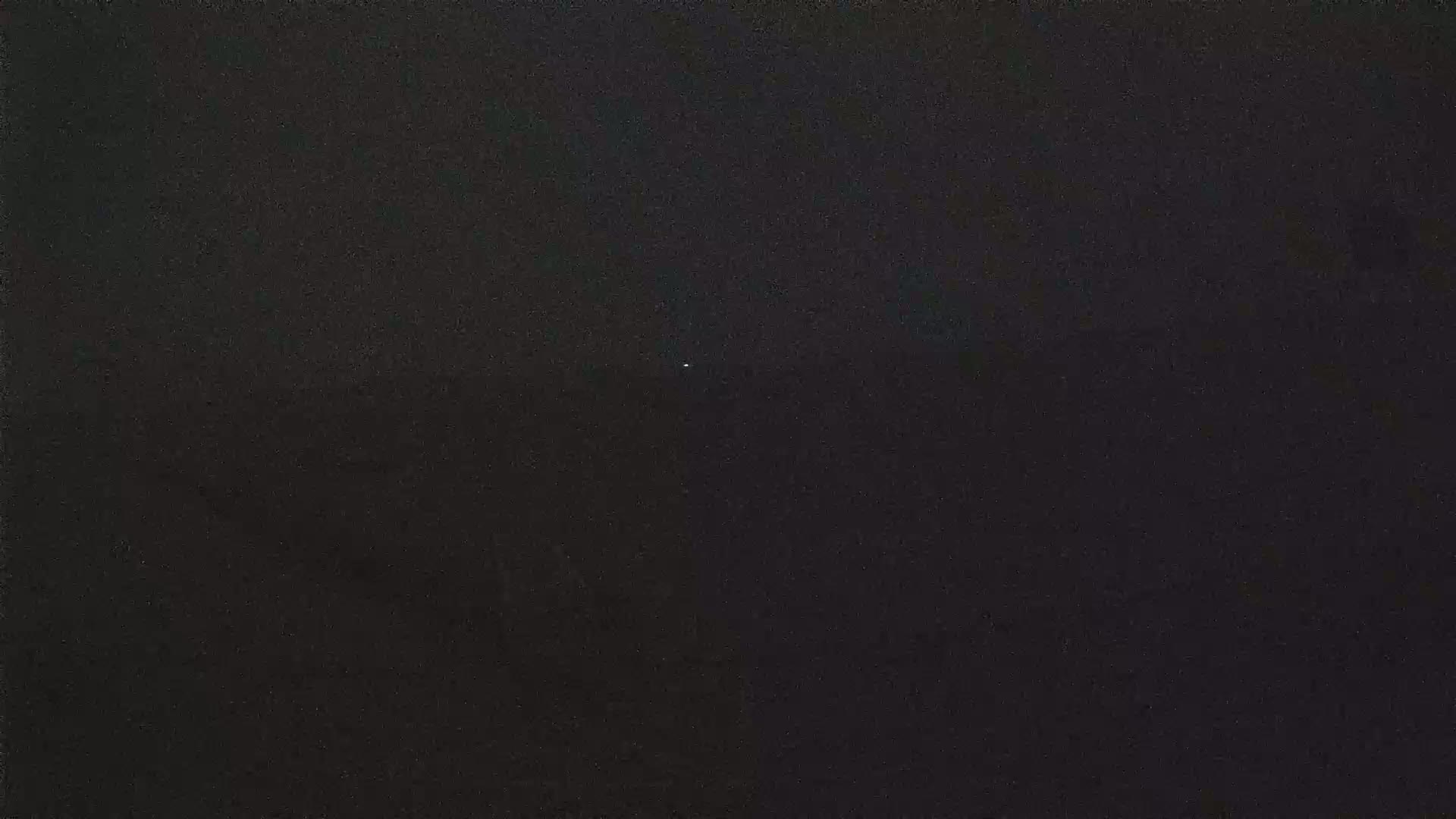 A single, faint light is visible in a dark, nighttime sky.
