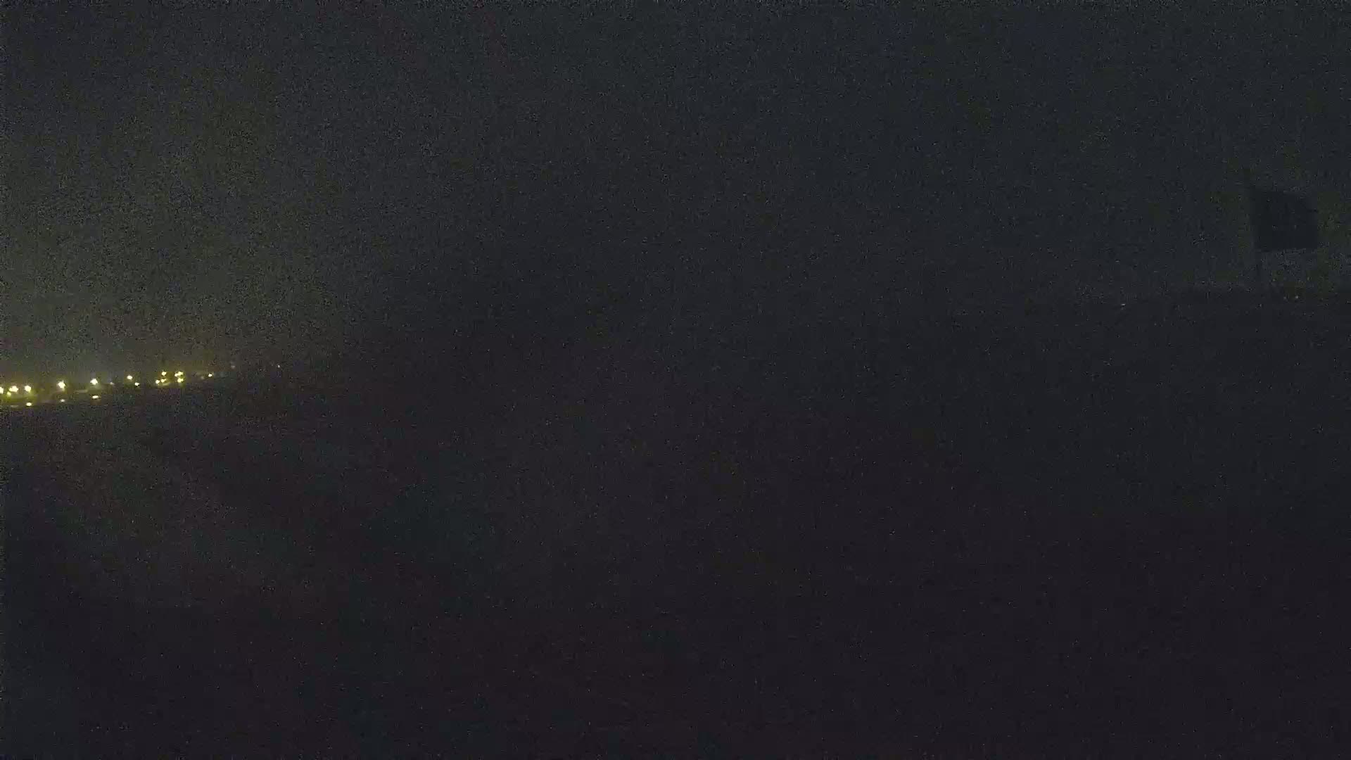 A dark, nighttime scene shows a distant line of faint lights and a mostly obscured foreground under a dark sky.