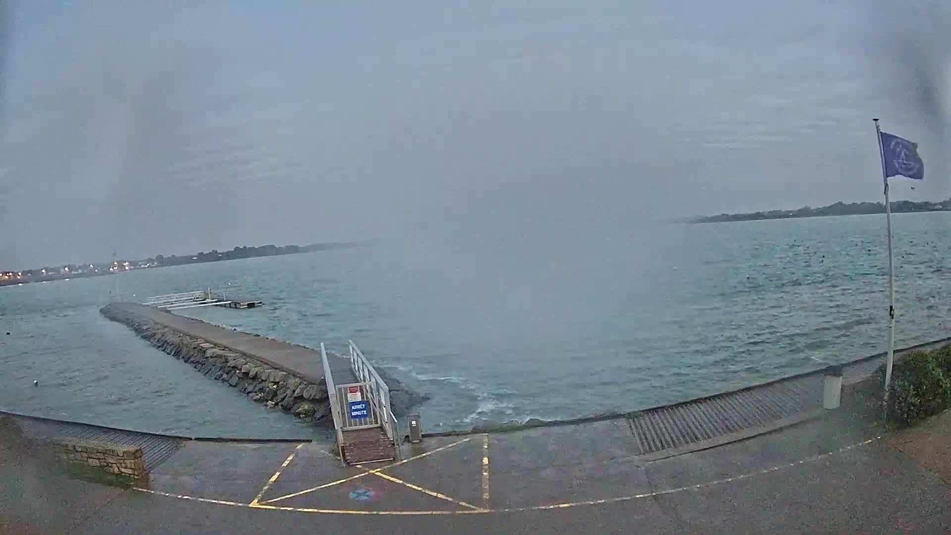 A stone jetty extends into a choppy, grey body of water under an overcast sky.