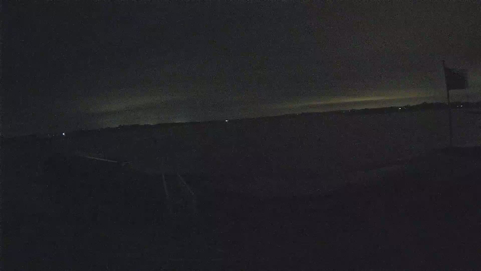 A dark, nighttime scene shows a body of water under a mostly clear sky with a flagpole visible in the right corner.