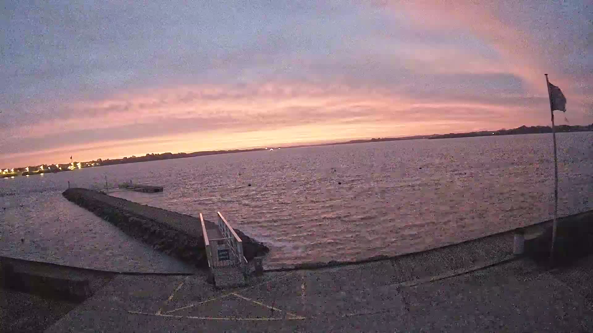 A calm body of water stretches to a distant shoreline under a pink and purple sunrise.
