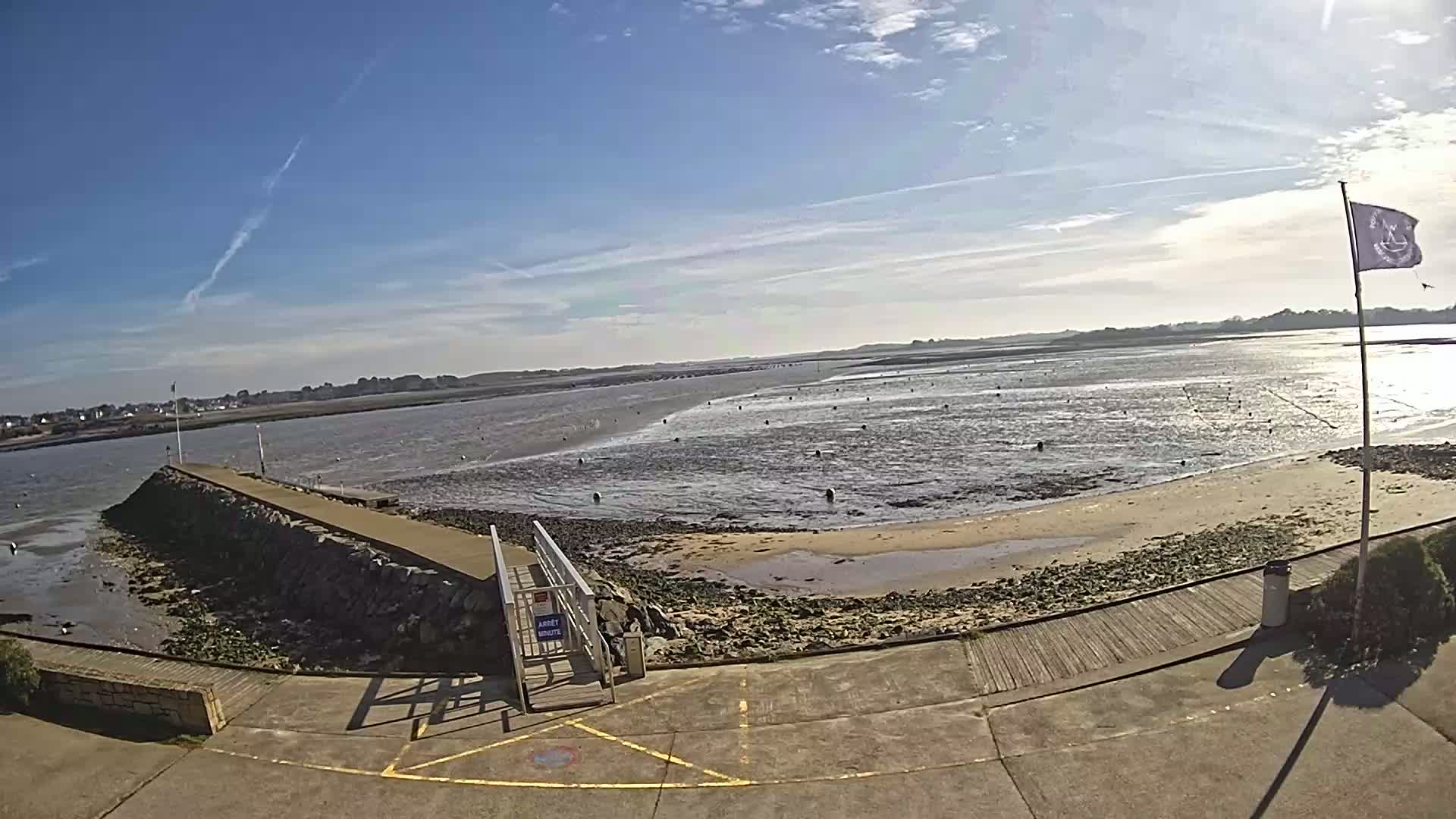 A stone jetty extends into a calm, shallow bay under a mostly sunny sky.