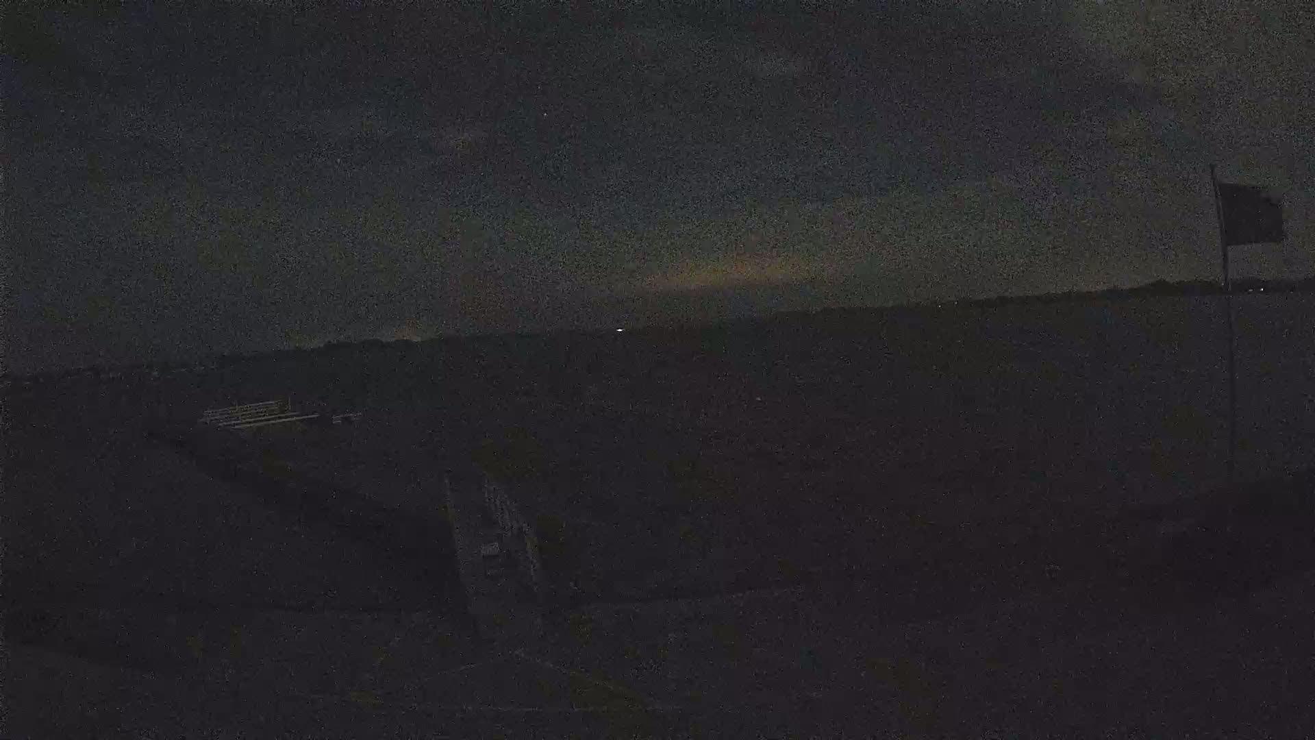A dark, nighttime scene shows a body of water under a mostly cloudy sky, with a flagpole and some indistinct structures visible in the foreground.