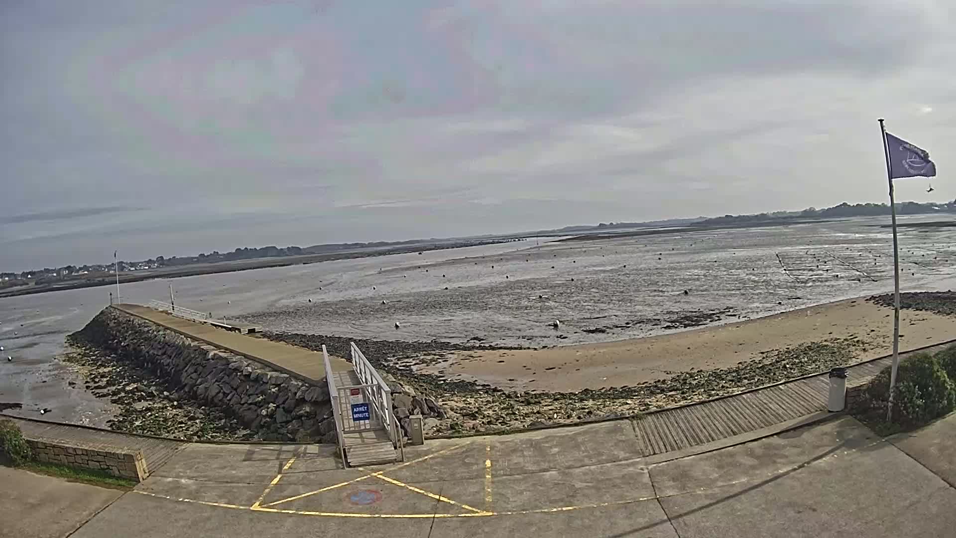 A stone jetty extends into a wide expanse of mudflats at low tide under an overcast sky.