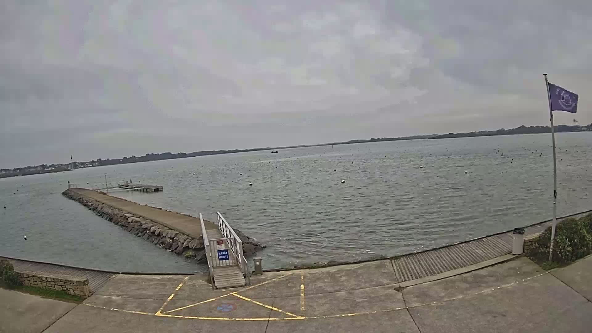 A long stone jetty extends into a calm, grey body of water under an overcast sky.
