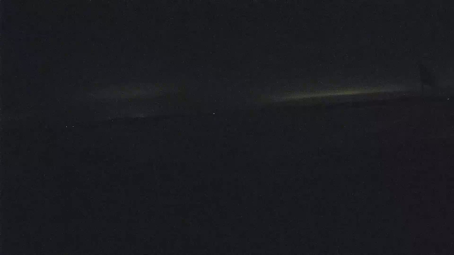 A dark, nighttime landscape is shown with a faint, horizontal light source on the horizon.