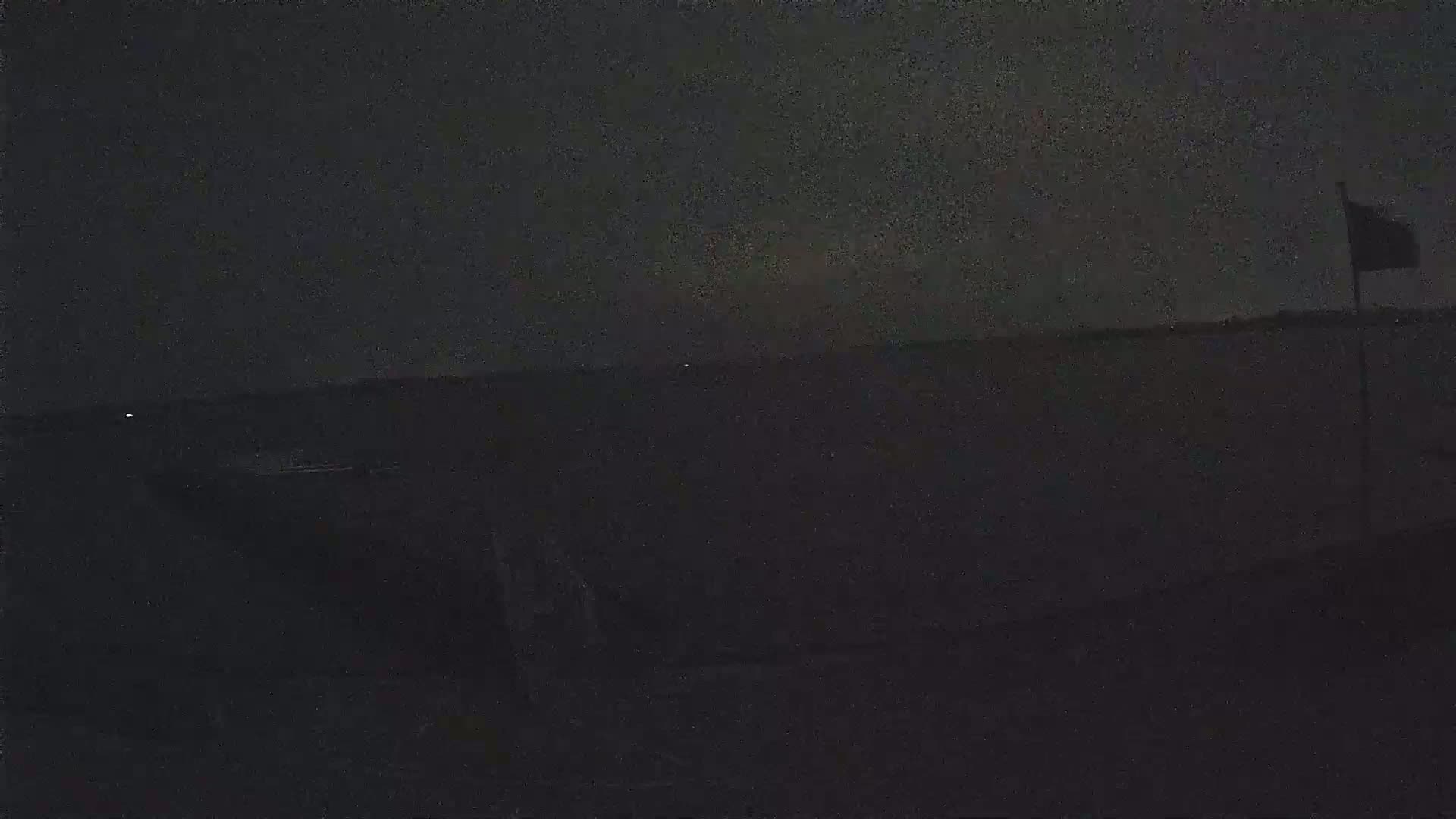 A dark, nighttime scene shows a body of water under a mostly clear, dark sky with a single flag visible in the distance.