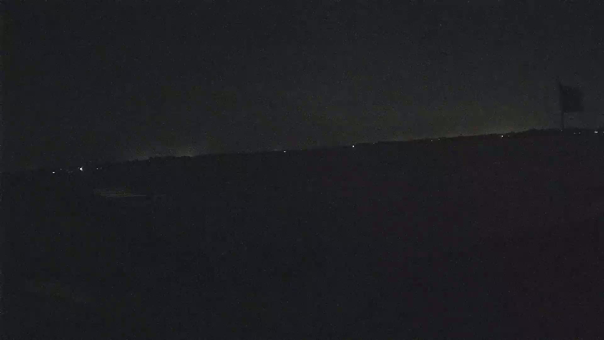 A dark, nighttime landscape is shown with a few faint lights in the distance under a clear, starless sky.