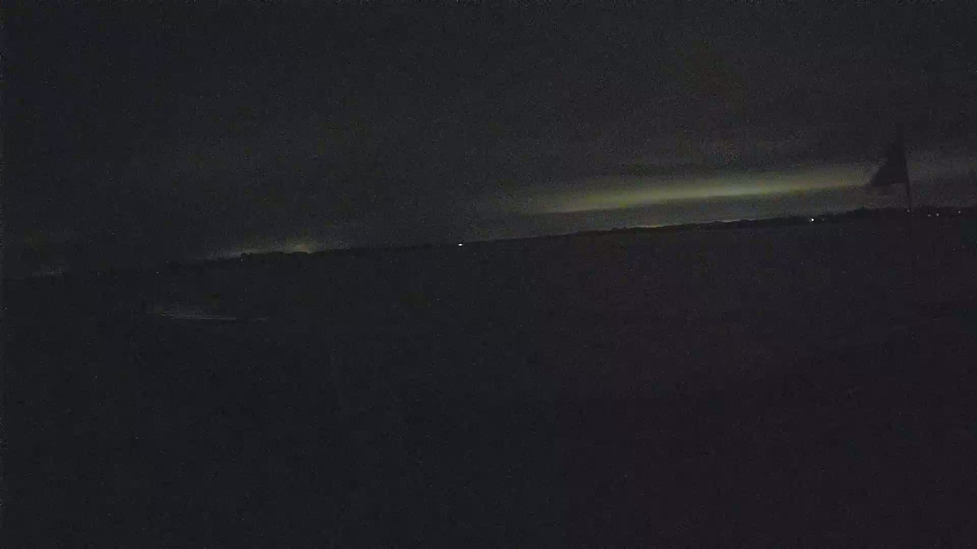 A dark, nighttime scene shows a flat, dimly lit landscape with a single flagpole visible in the distance under a mostly clear sky.