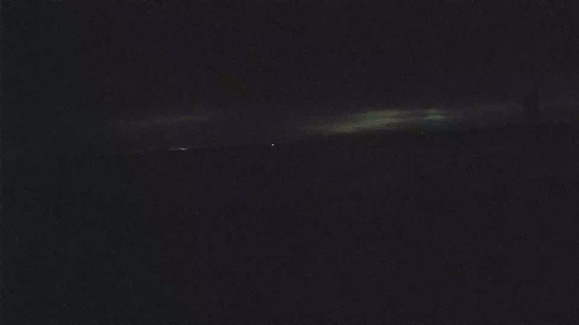 A dark, nighttime landscape shows a faint, pale band of clouds near the horizon.