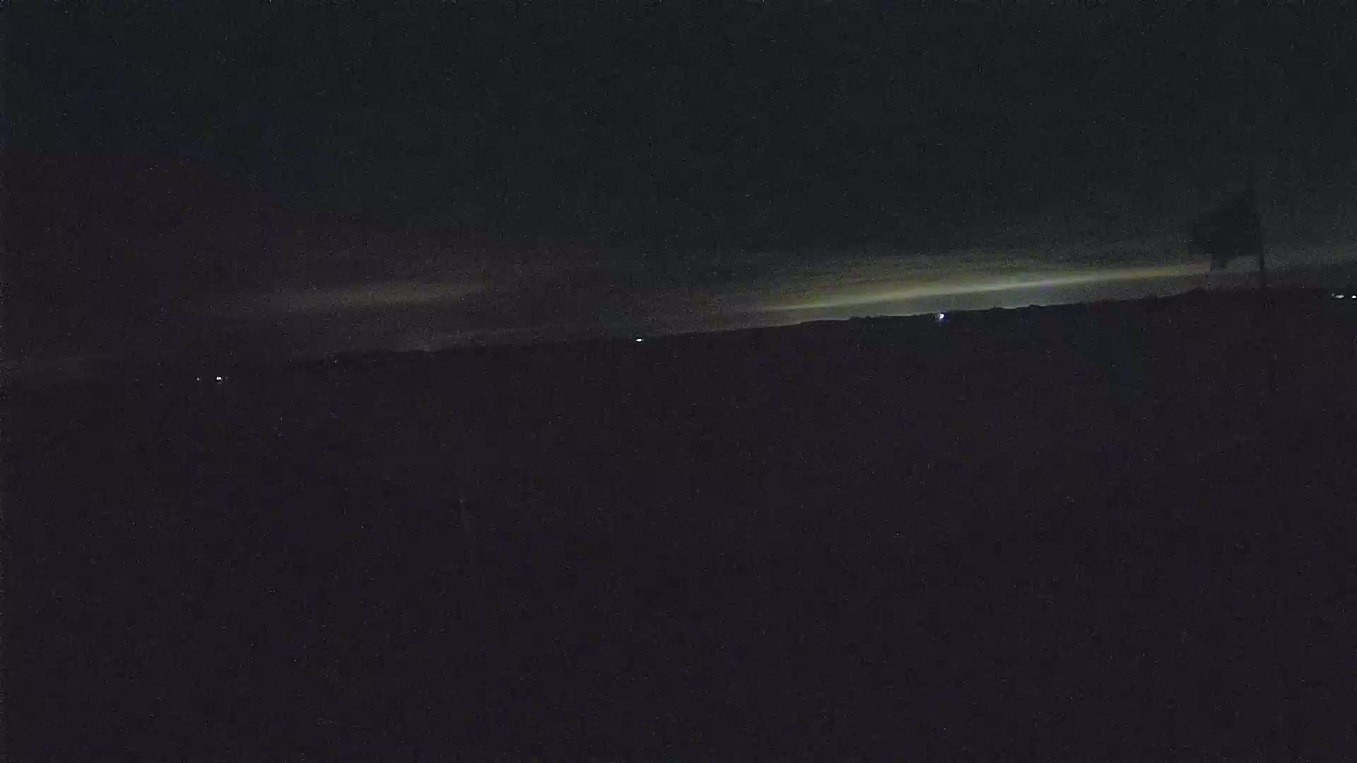 A dark, nighttime landscape is shown with a faint, light-colored horizon line in the distance.