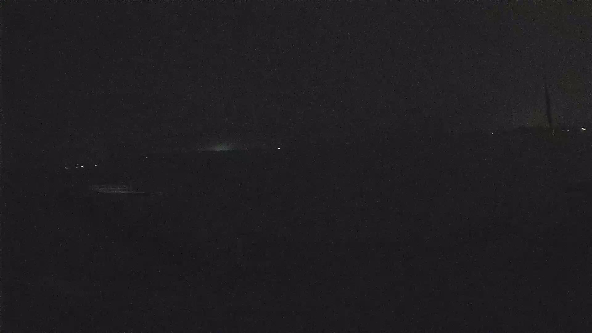 A dark, nighttime landscape is shown, with a faint, low light source on the horizon.