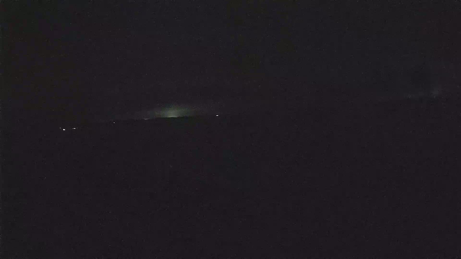 A dark, nighttime landscape is visible with a faint, low-lying light source on the horizon.