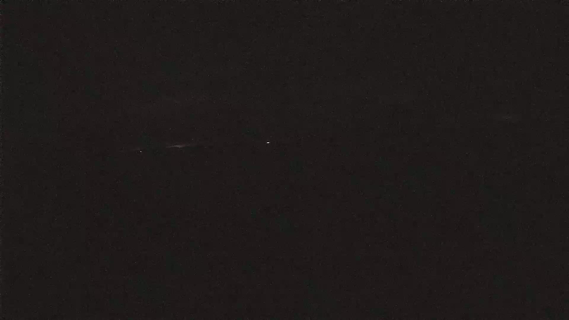 A dark, nighttime scene shows a faint horizontal light in the distance with two brighter lights slightly below it.