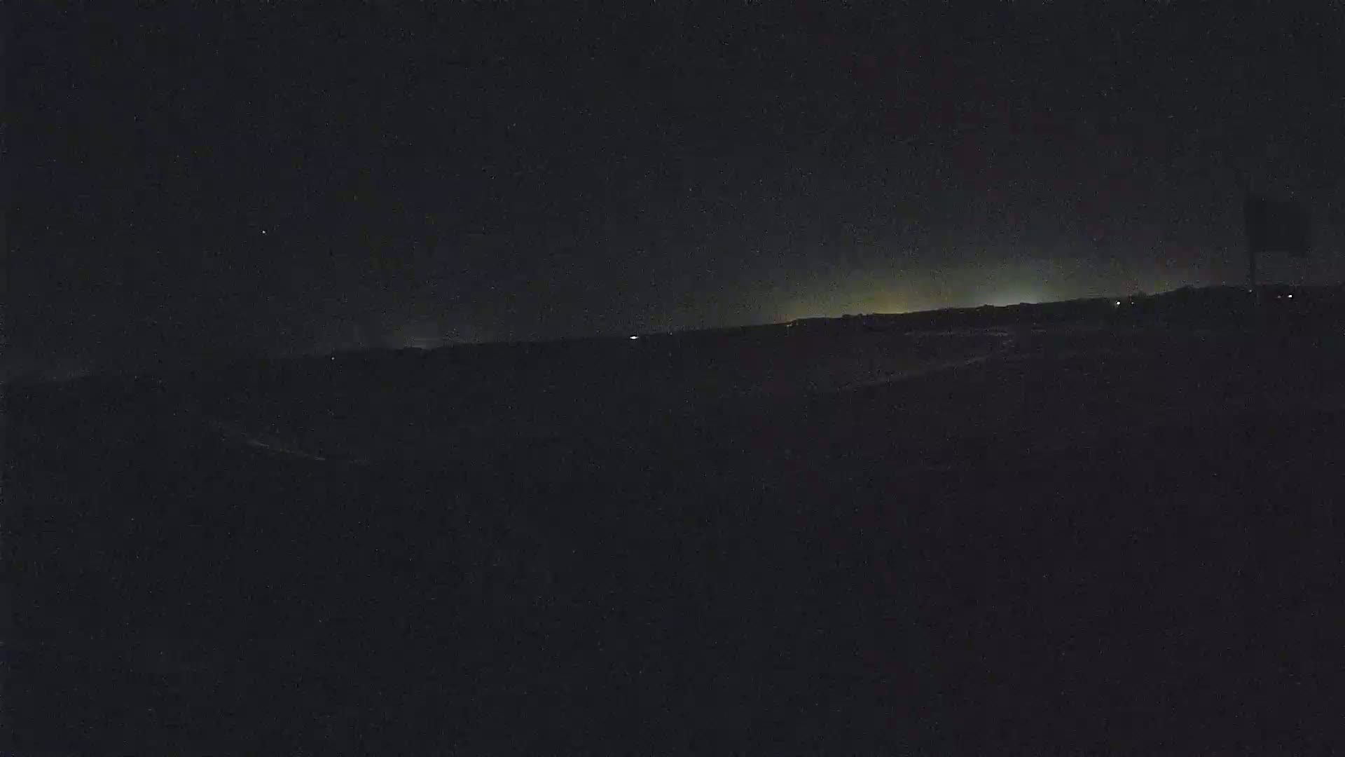 A dark, nighttime landscape shows a distant, faintly lit horizon under a clear, starlit sky.