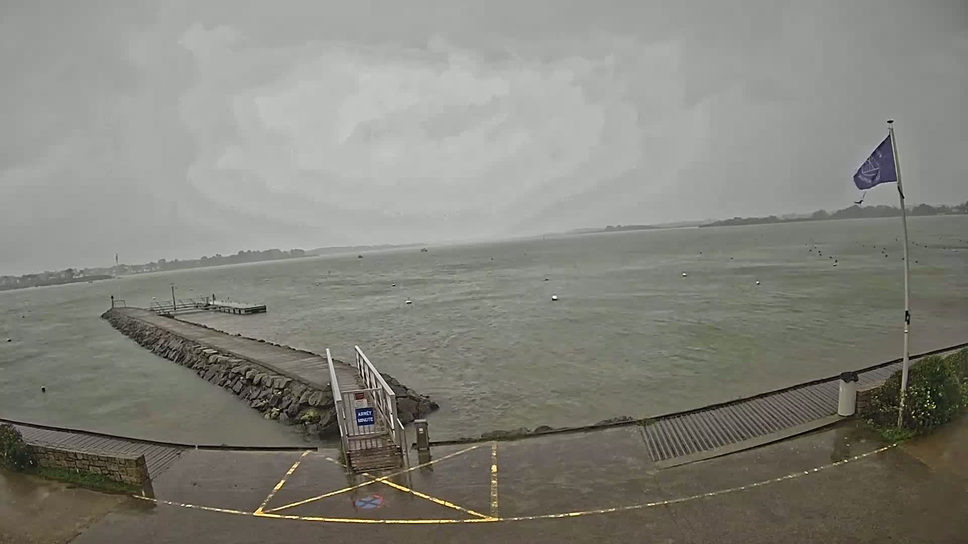 A stone pier extends into a choppy gray body of water under an overcast sky.