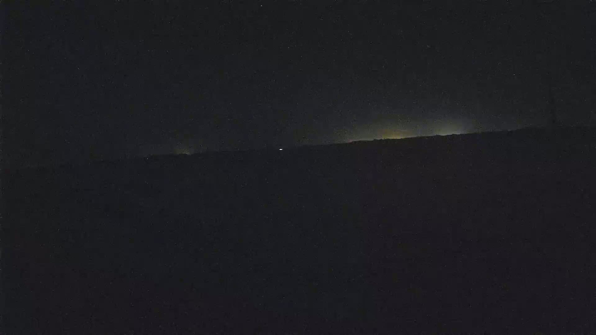 A dark, nighttime landscape shows a faintly lit horizon under a starlit sky.