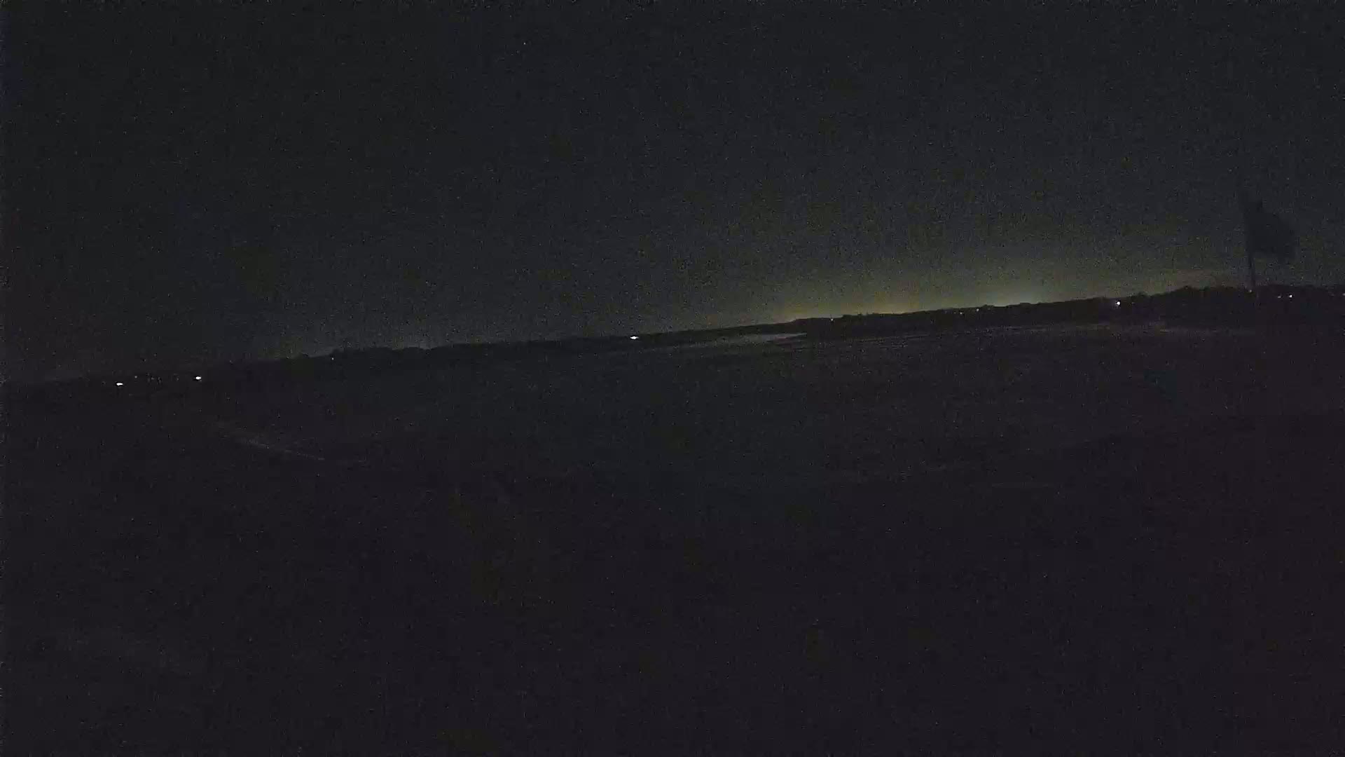 A dark, nighttime landscape is visible, with a faintly illuminated horizon line under a mostly clear, dark sky.