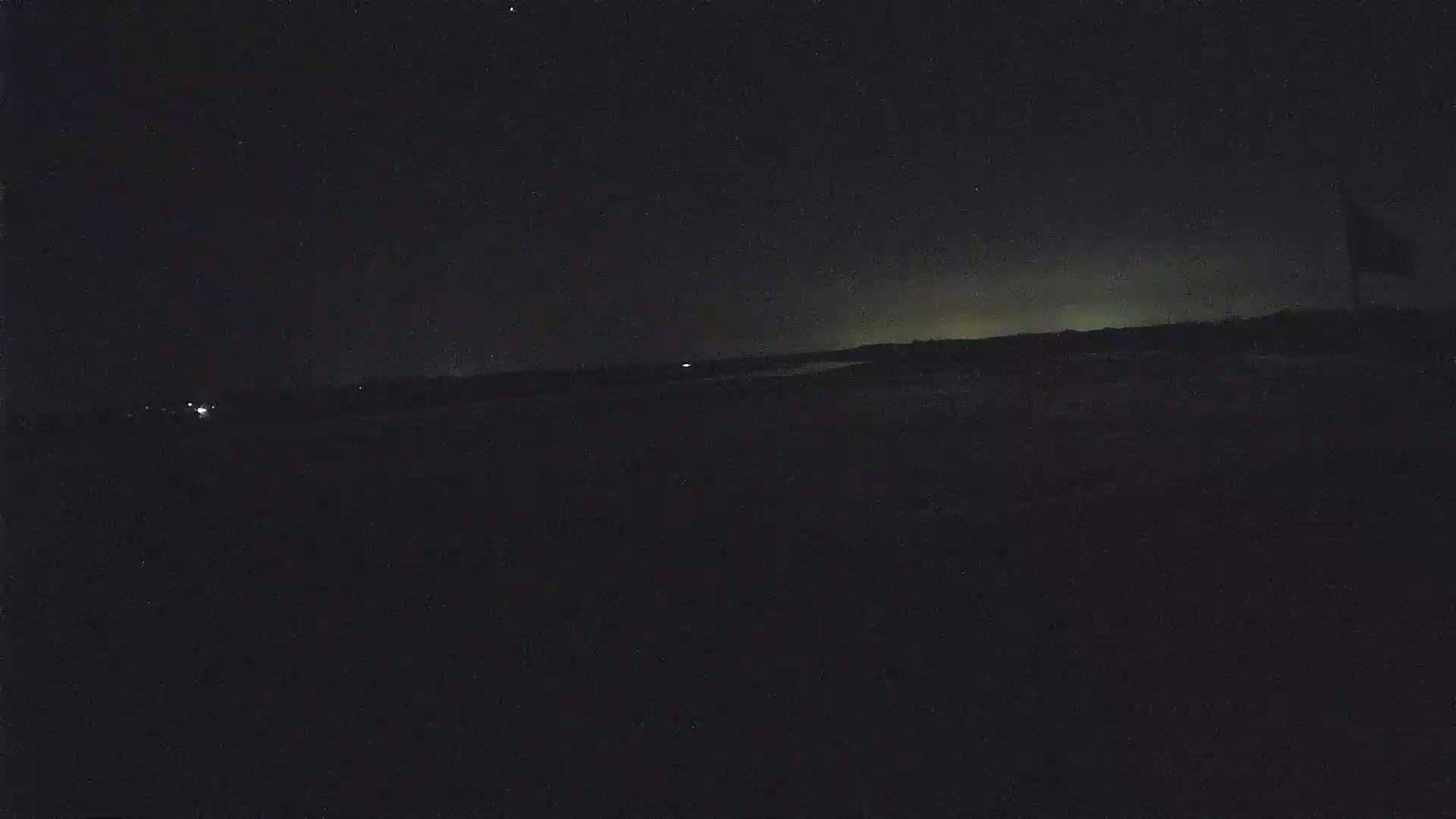 A dark, nighttime landscape is visible, showing a flat horizon with a few distant lights under a mostly clear, starry sky.