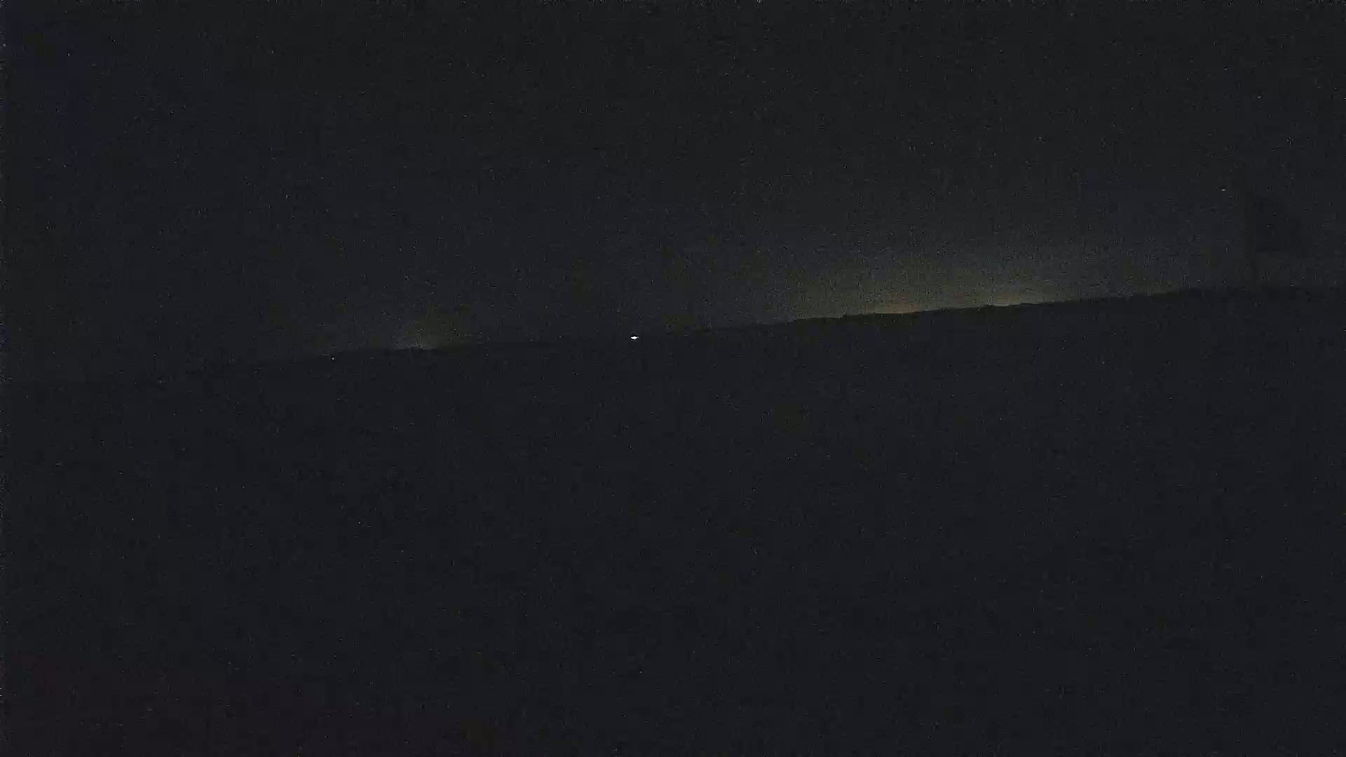 A dark, nighttime landscape is shown, with a faint, light horizon line visible.