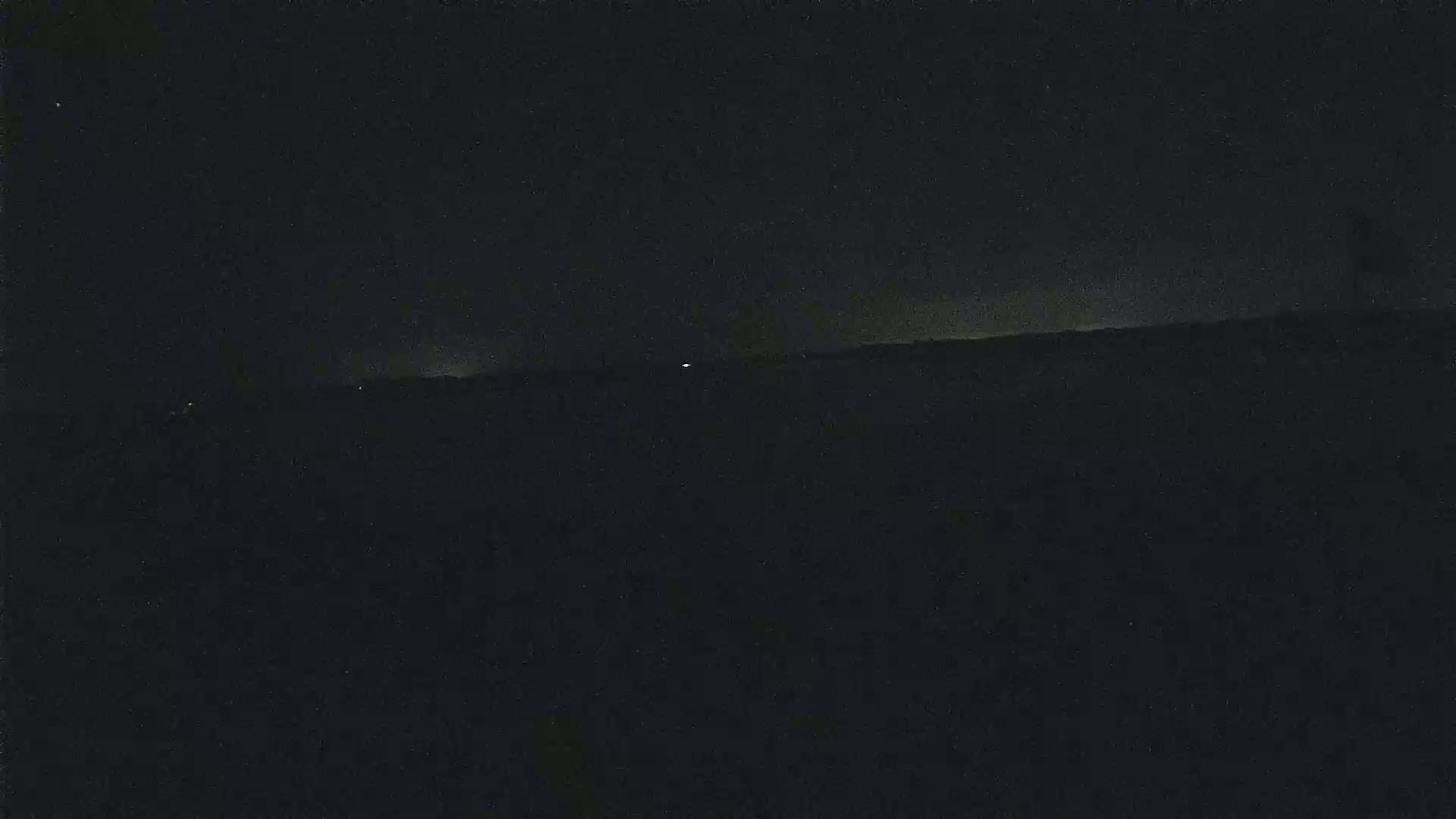 A dark, nighttime landscape shows a distant horizon line with a few faint lights.