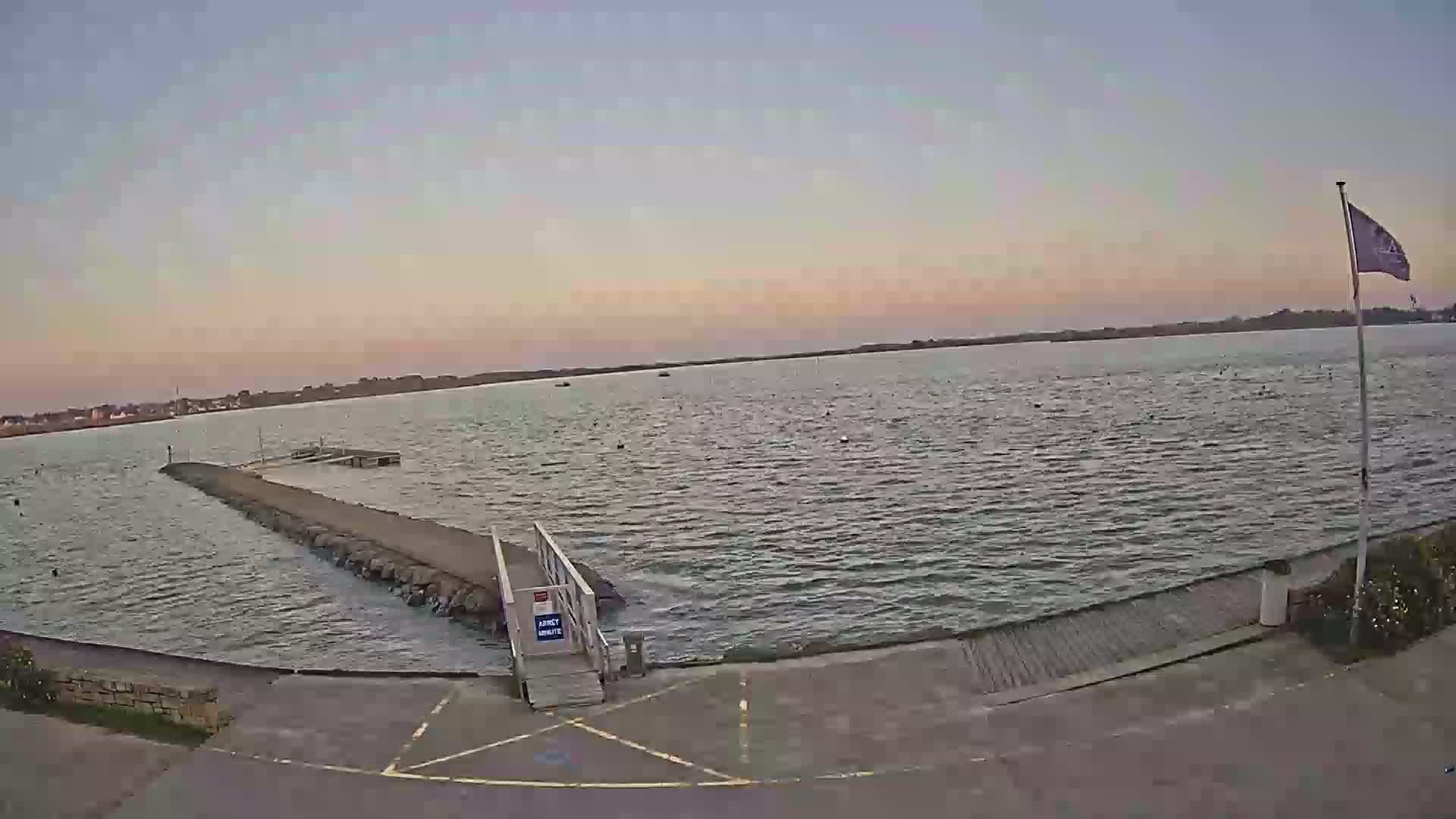 A calm body of water with a small pier and a flagpole under a dusky, pinkish sky.