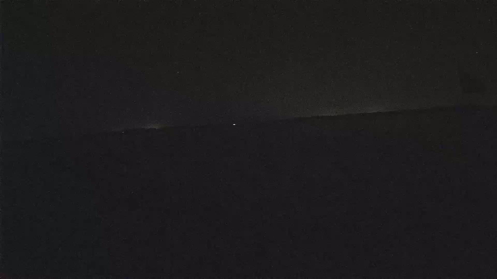 A dark, nighttime landscape is visible, with a few faint lights in the distance under a mostly clear sky.