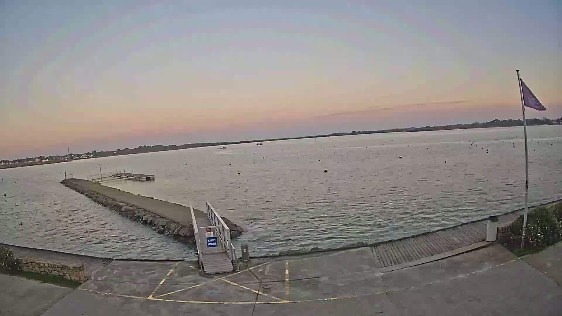 A calm body of water at sunset is seen from a dock with a small ramp leading to the water.