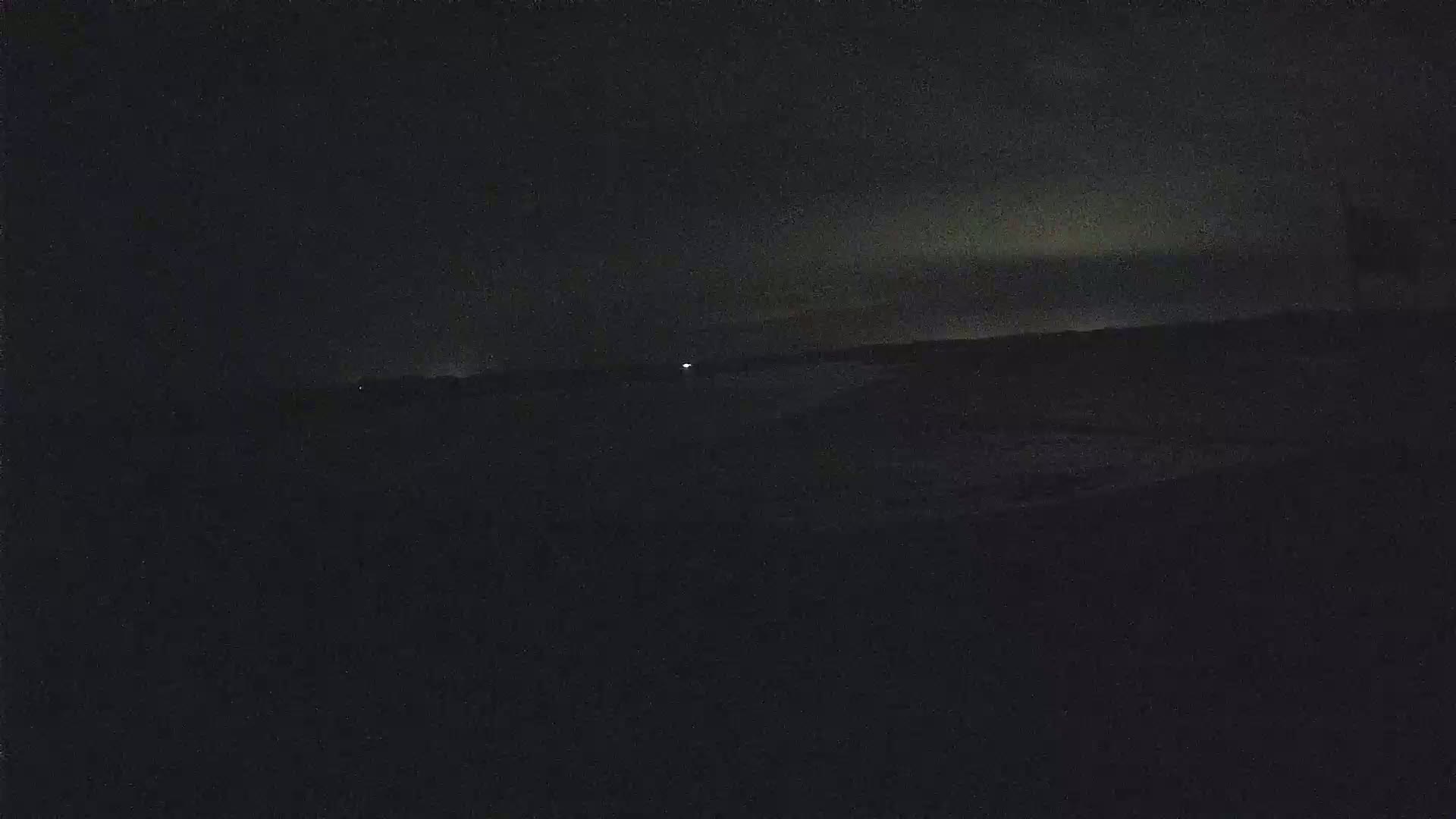 A dark, nighttime landscape is visible, with a faint glow on the horizon under a mostly clear sky.