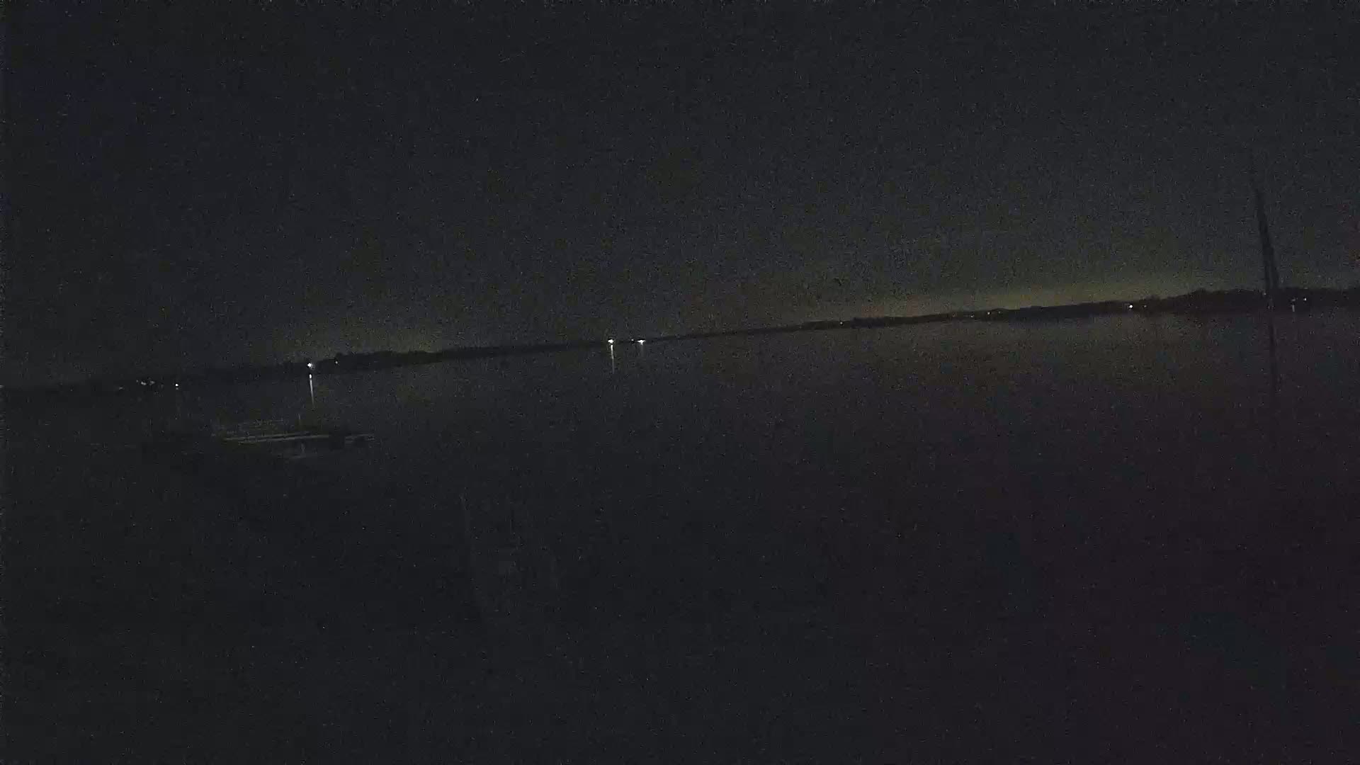 A dark, nighttime view of a calm body of water with a few distant lights on the far shore.