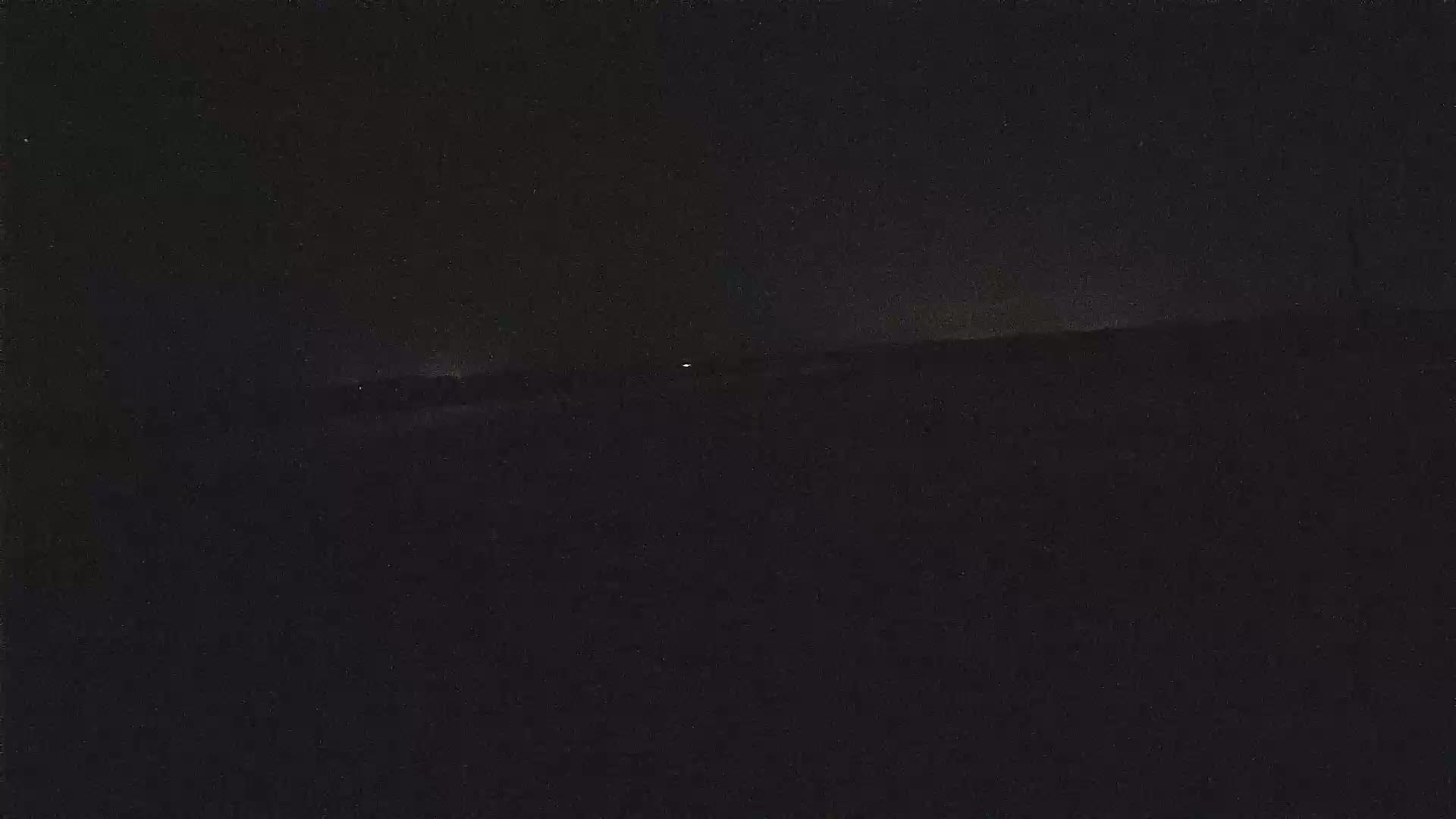 A dark, nighttime landscape is visible, with a few faint lights in the distance.