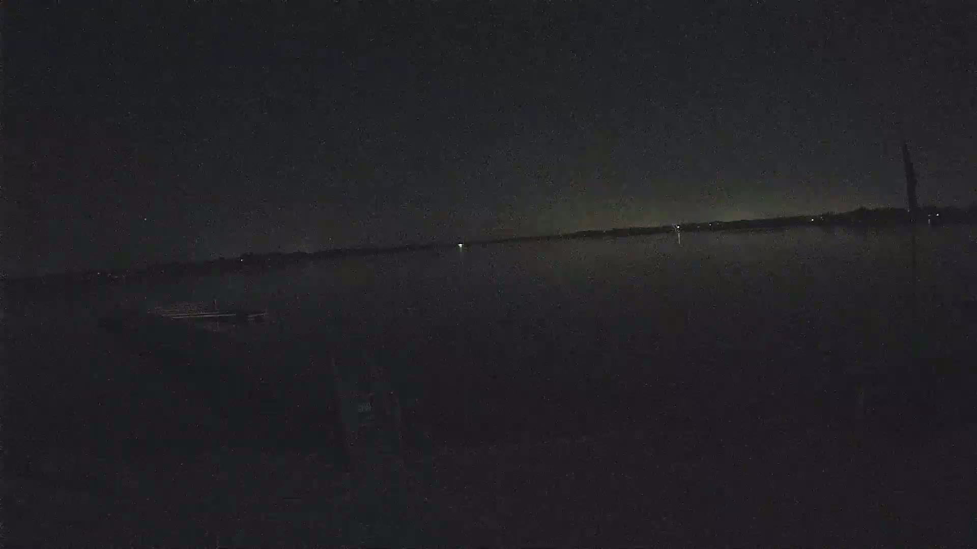 A dark, still body of water is visible under a night sky speckled with stars, with a small boat or dock barely visible near the bottom.