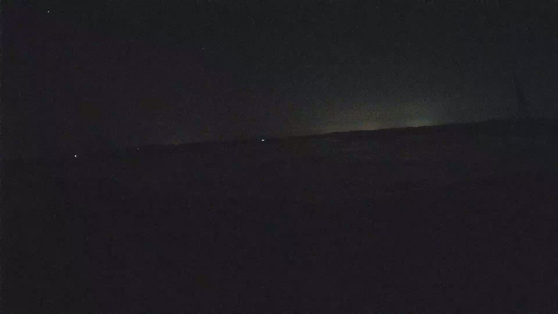 A dark, nighttime landscape is visible, with a few faint lights in the distance.