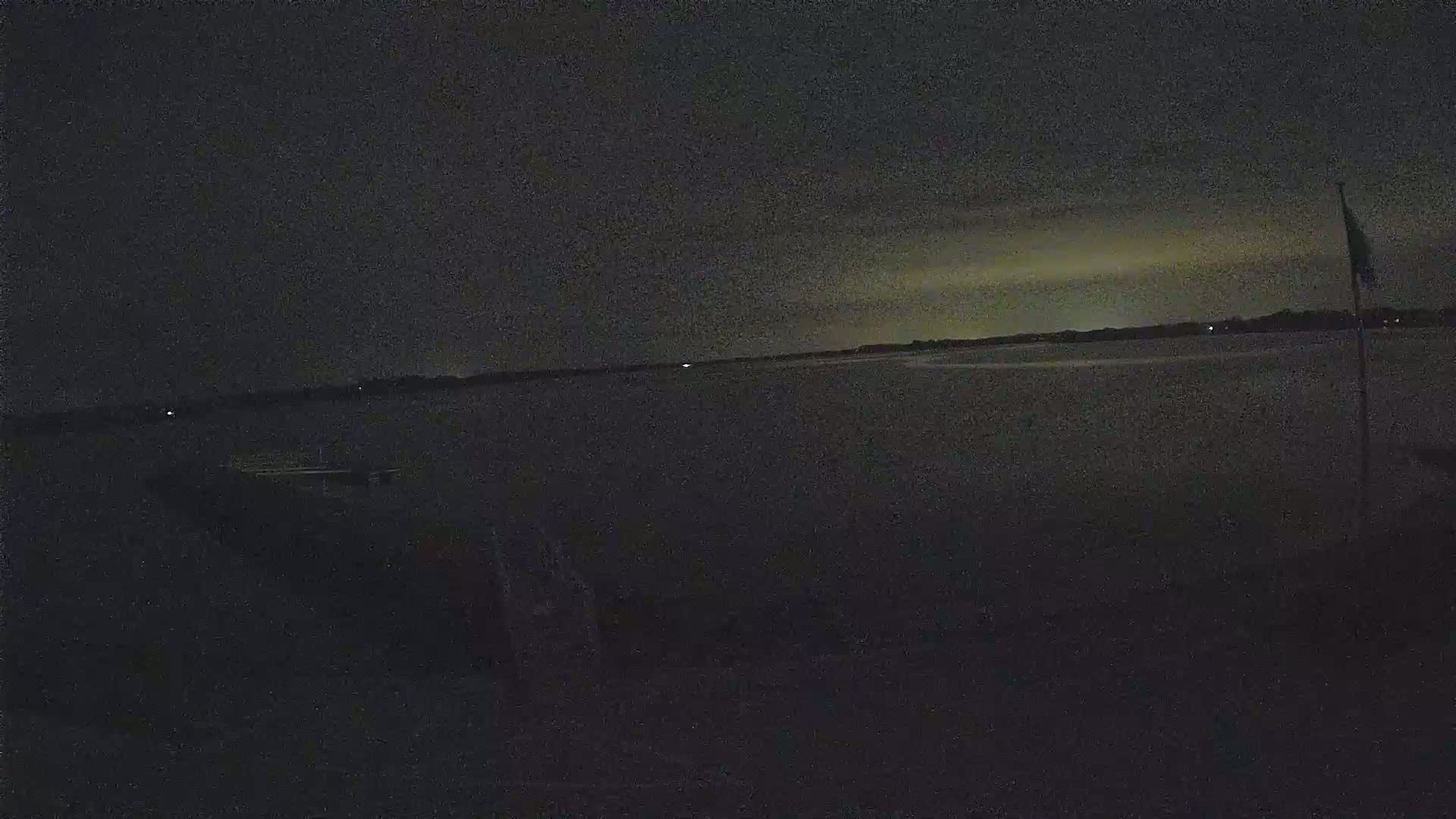A dark, nighttime view of a body of water with a faintly lit horizon under a mostly cloudy sky.