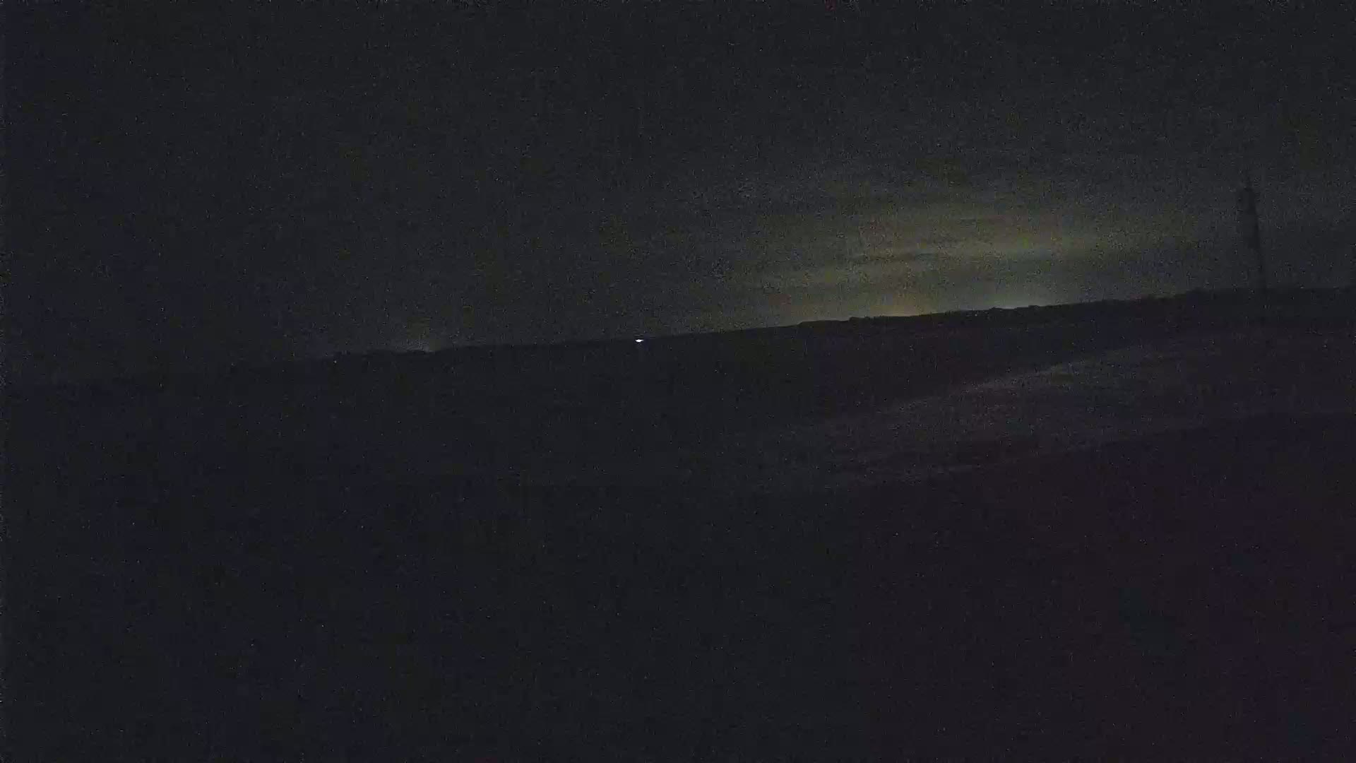 A dark, nighttime landscape is visible, with a faint, light horizon and a single, distant light source.