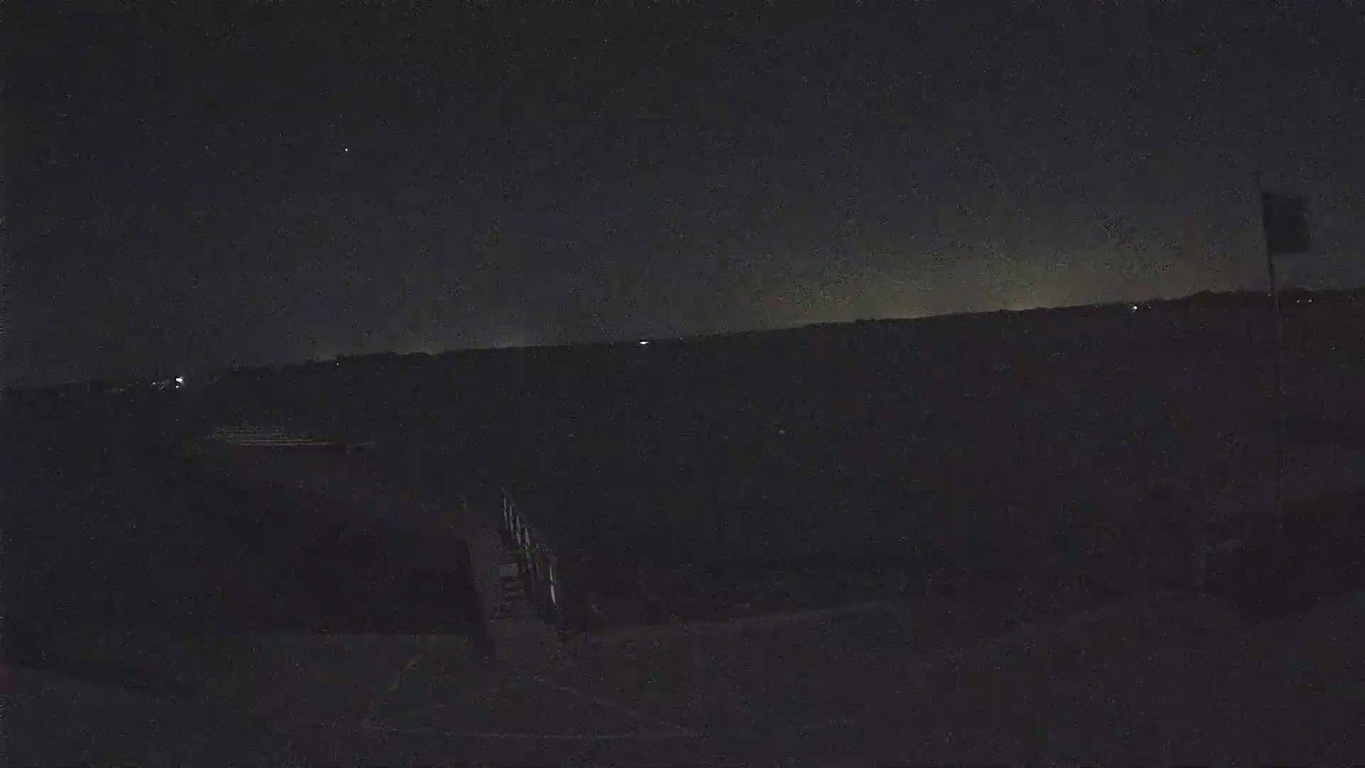 A nighttime view shows a dark, flat landscape under a mostly clear, starry sky.