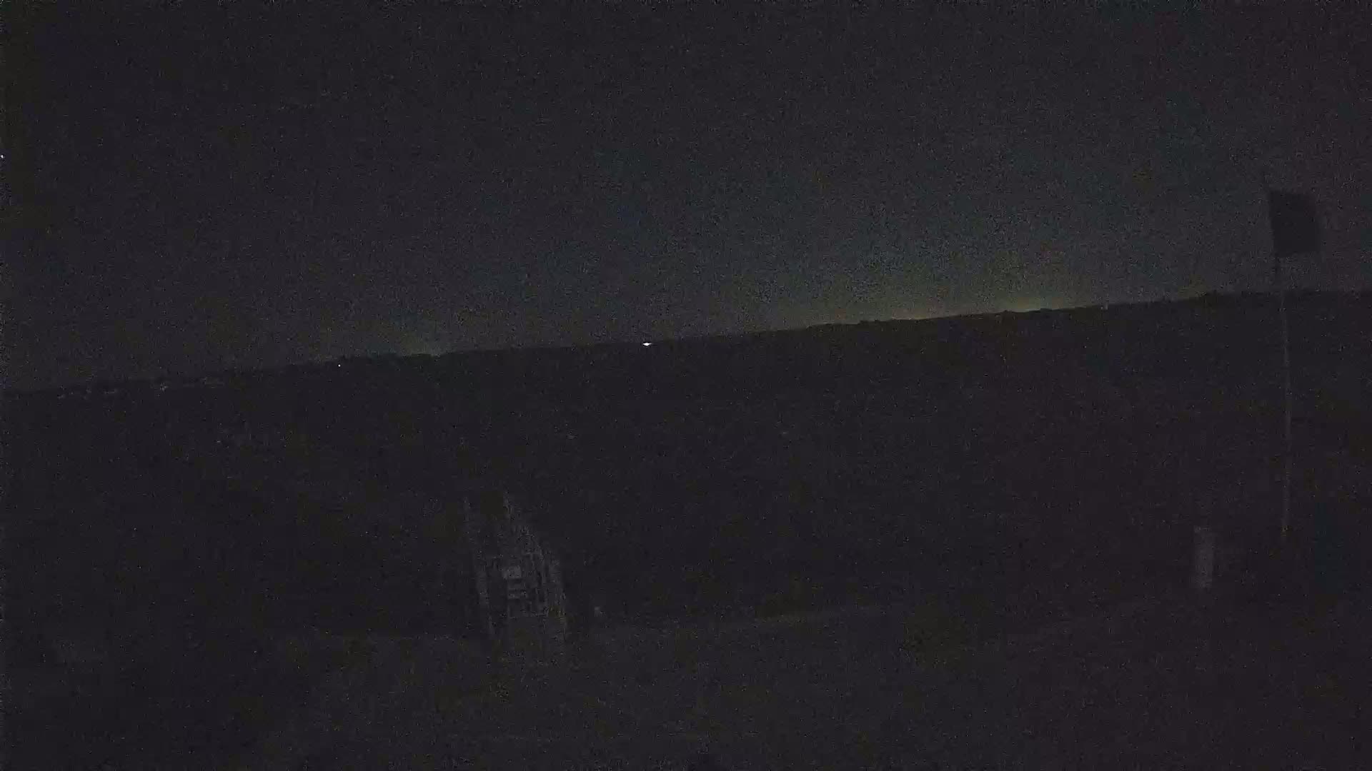 A dark, nighttime scene shows a mostly obscured landscape under a clear, dark sky with a faint horizon glow.