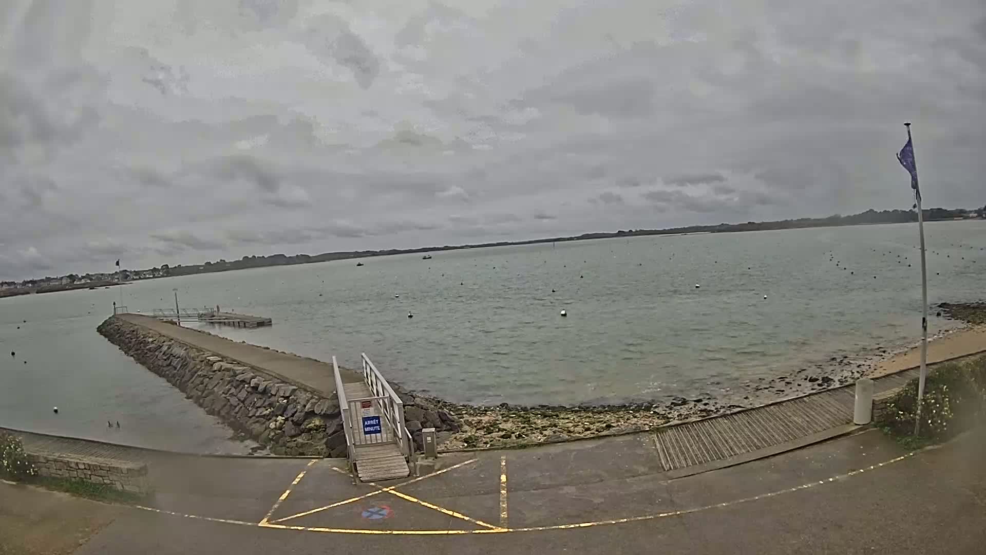A stone jetty extends into a calm, gray body of water under an overcast sky.