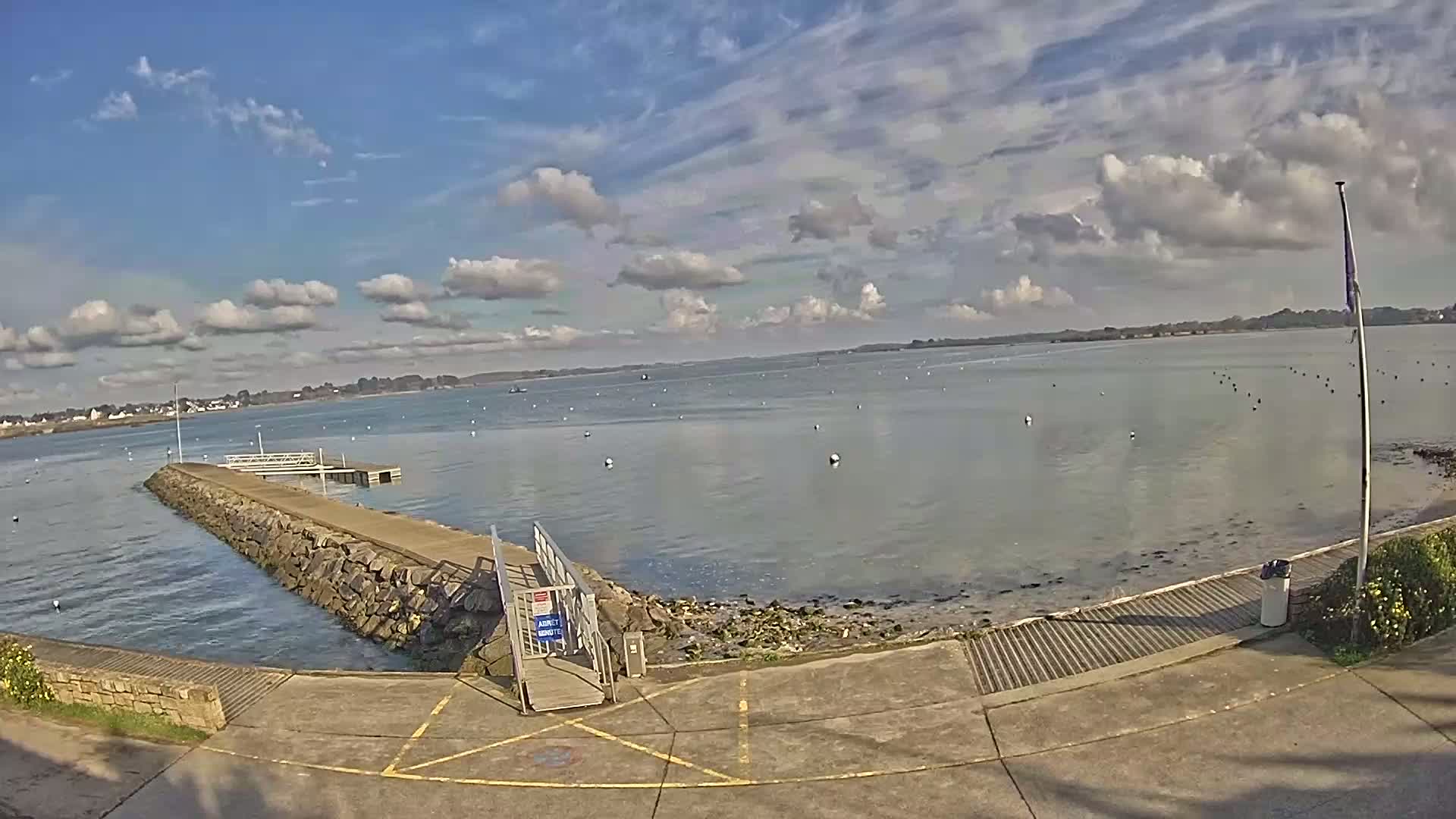 A stone pier extends into a calm body of water under a partly cloudy sky.