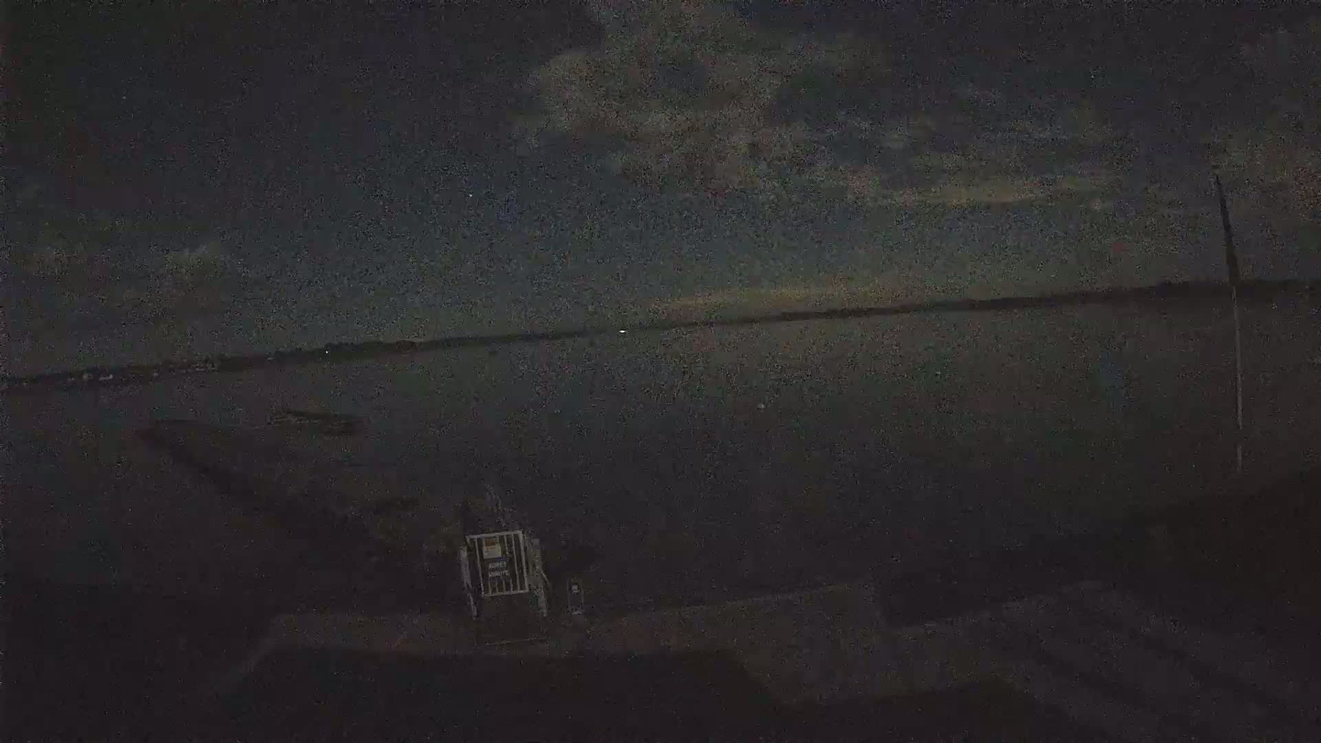 A dark, nighttime view of a calm body of water under a mostly cloudy sky.