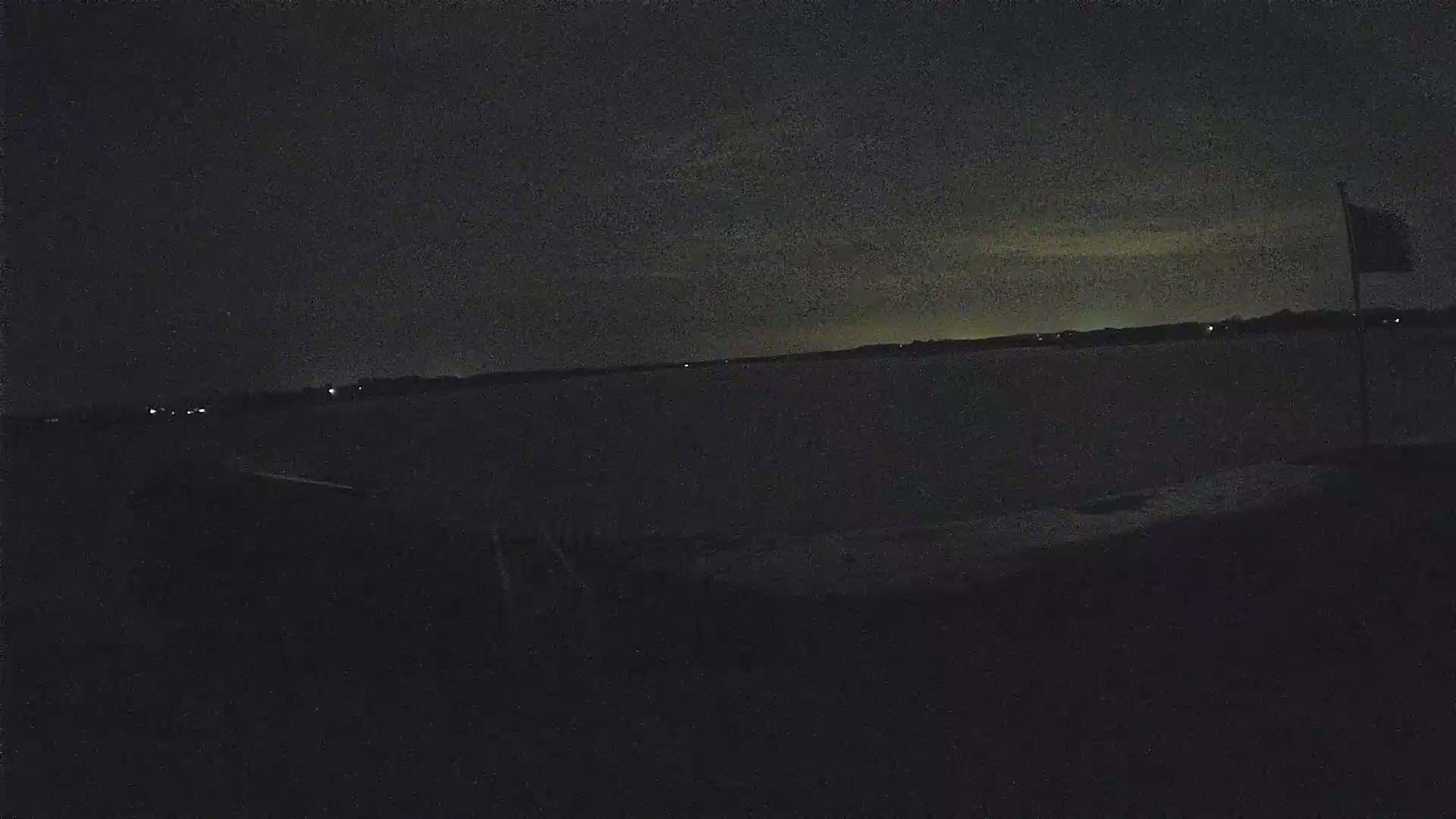 A dark, nighttime scene shows a body of water under a slightly cloudy sky, with a flagpole visible on the right.