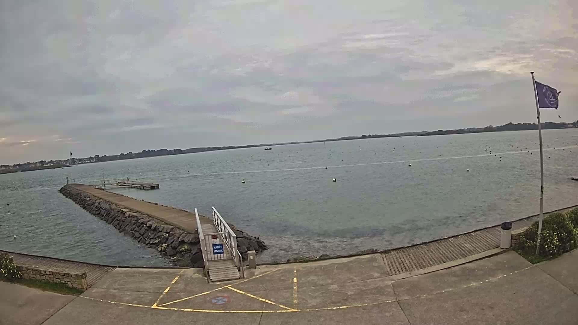 A stone jetty extends into a calm body of water under an overcast sky.