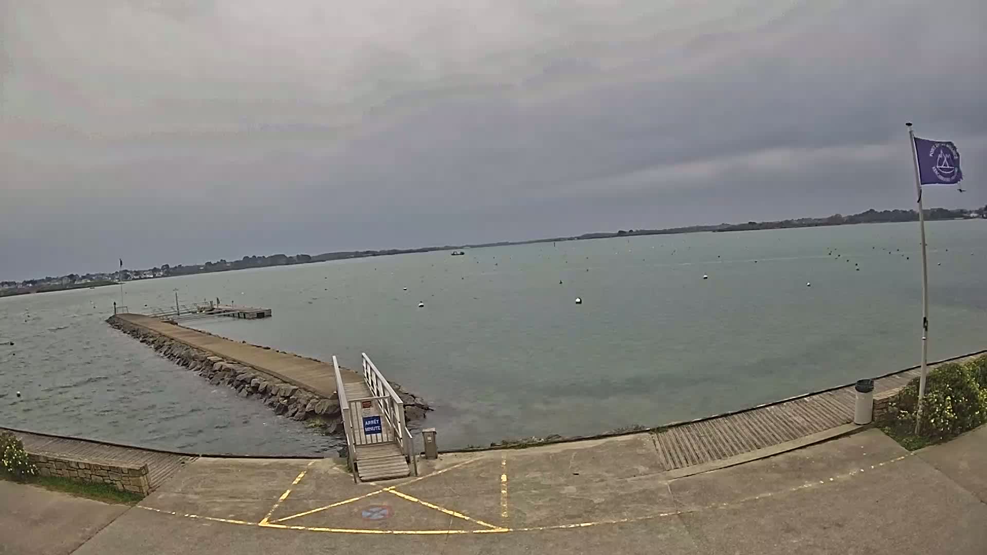 A long, stone pier extends into a calm, grey body of water under an overcast sky.