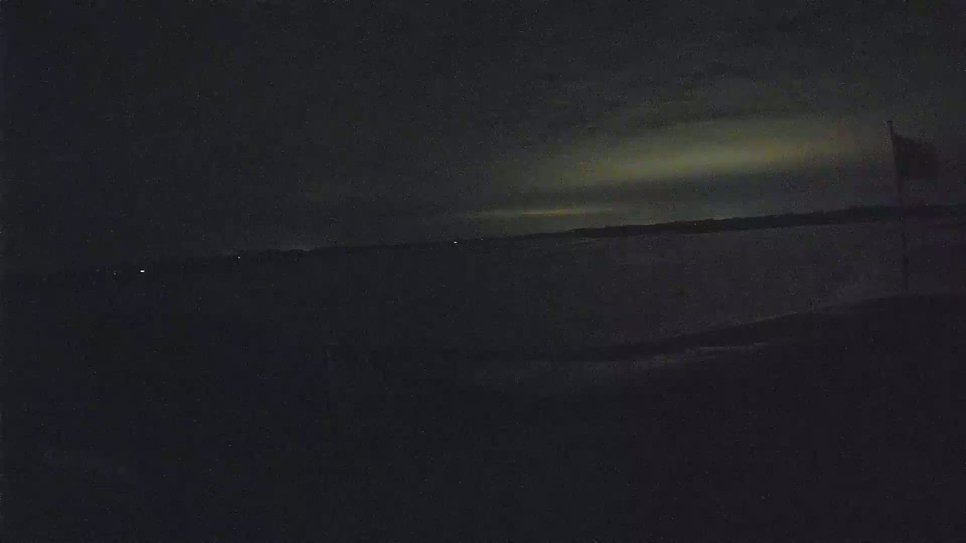 A dark nighttime scene shows a body of water under a faintly illuminated sky with a flagpole on the right.