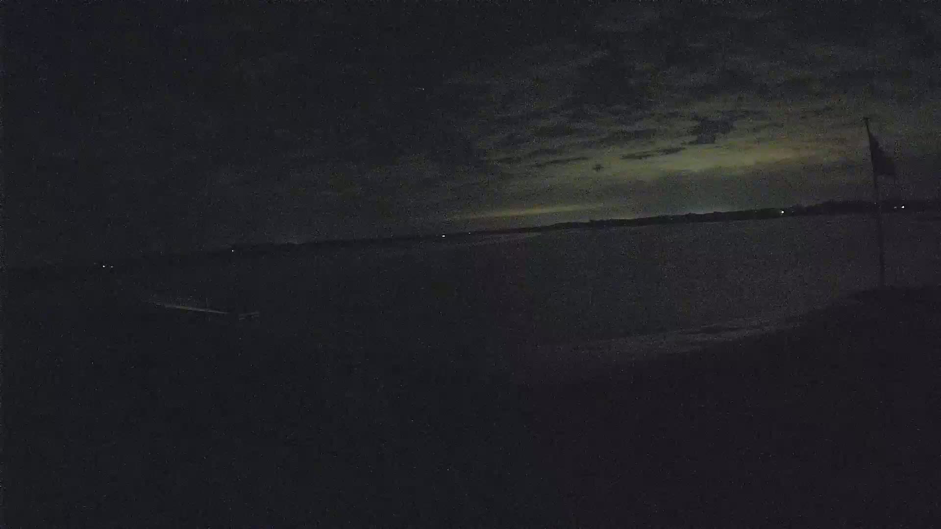 A dark, nighttime scene shows a body of water under a cloudy sky, with a flagpole visible on the right.
