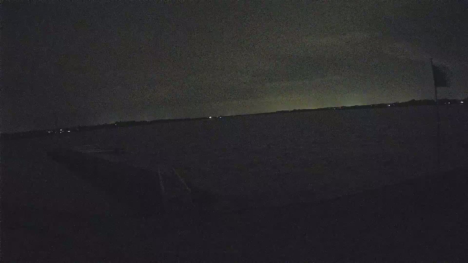 A dark body of water is visible under a night sky, with a faint shoreline and a few distant lights in the background.