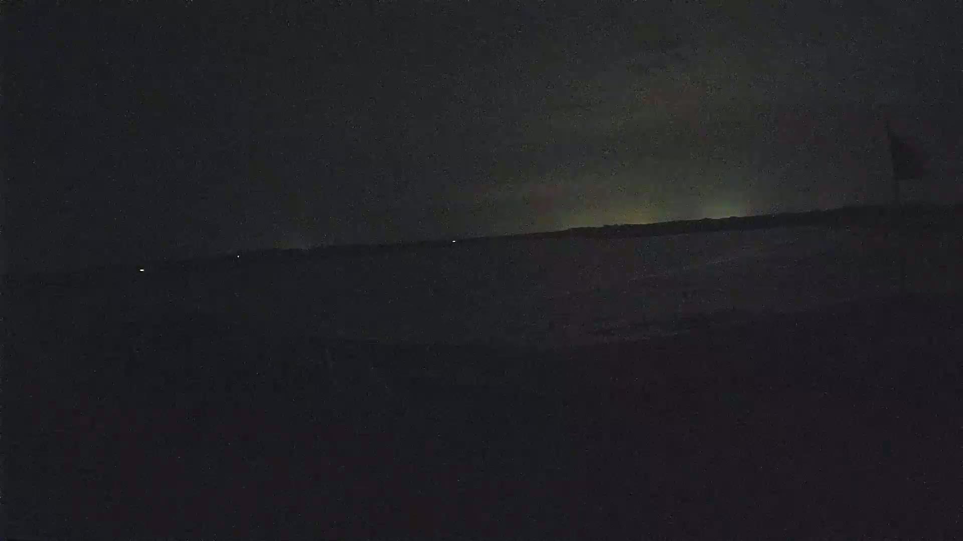 A dark, nighttime scene shows a distant, faintly lit horizon over a body of dark water.
