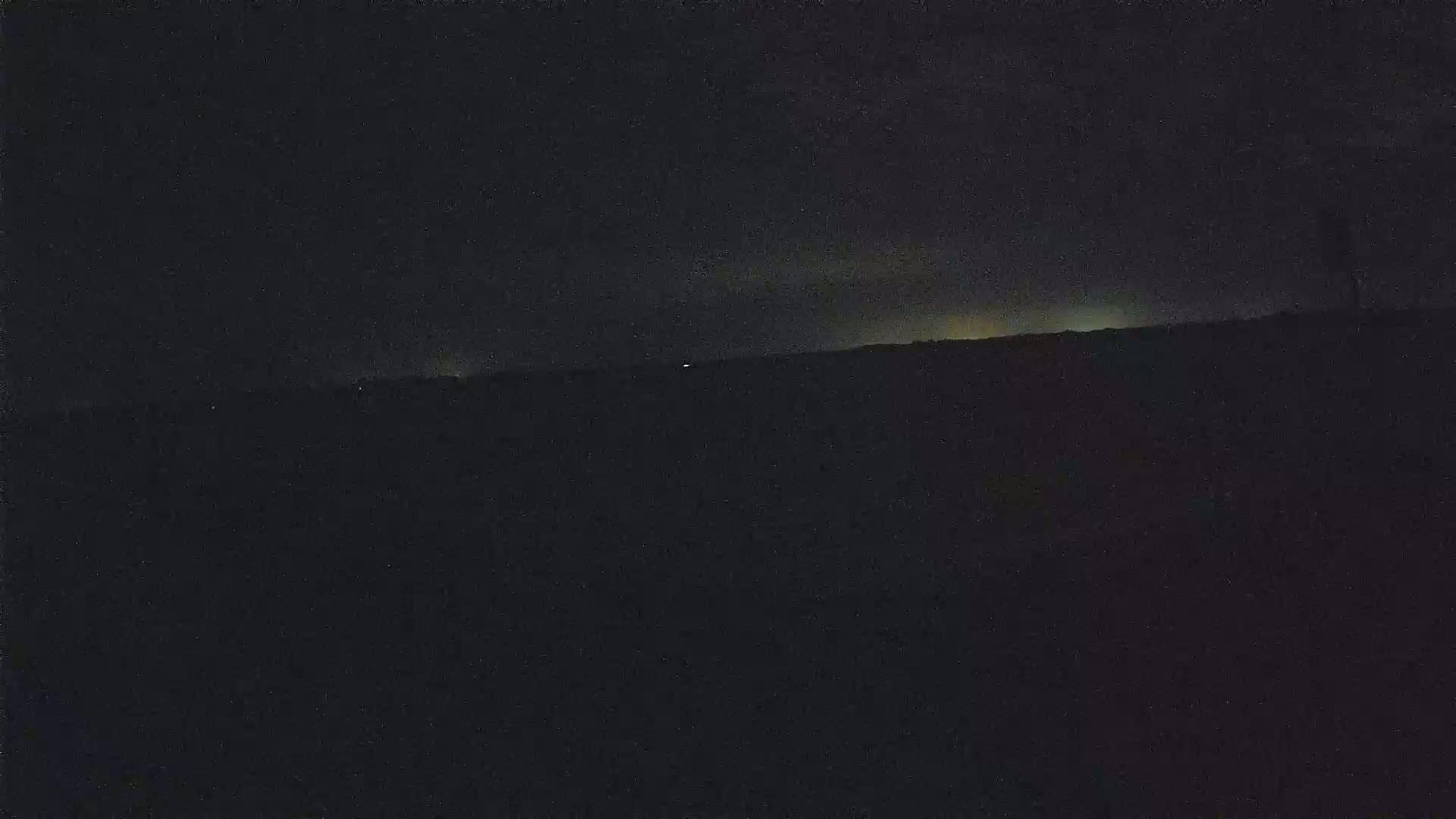 A dark, nighttime landscape shows a faintly lit horizon under a mostly clear sky.