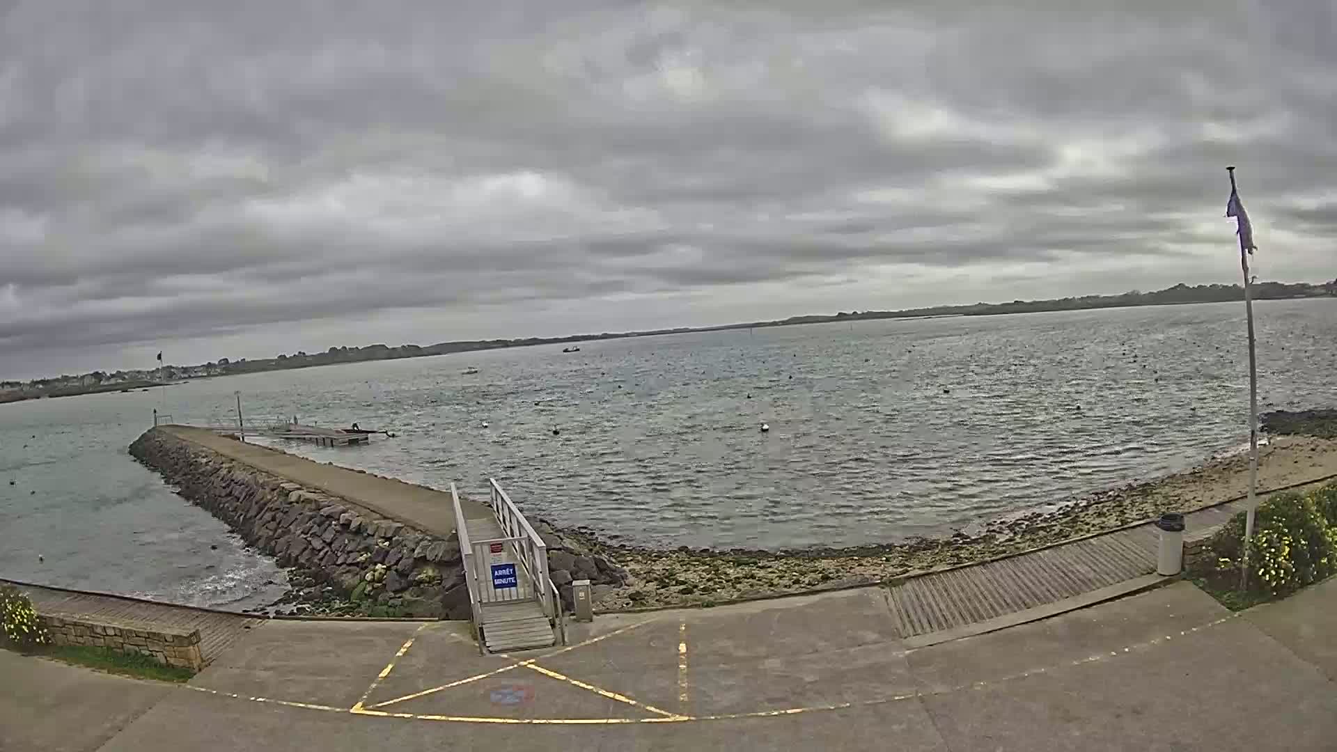 A rocky jetty extends into a calm, grey-sky day over a body of water with a small wooden ramp leading to the shore.