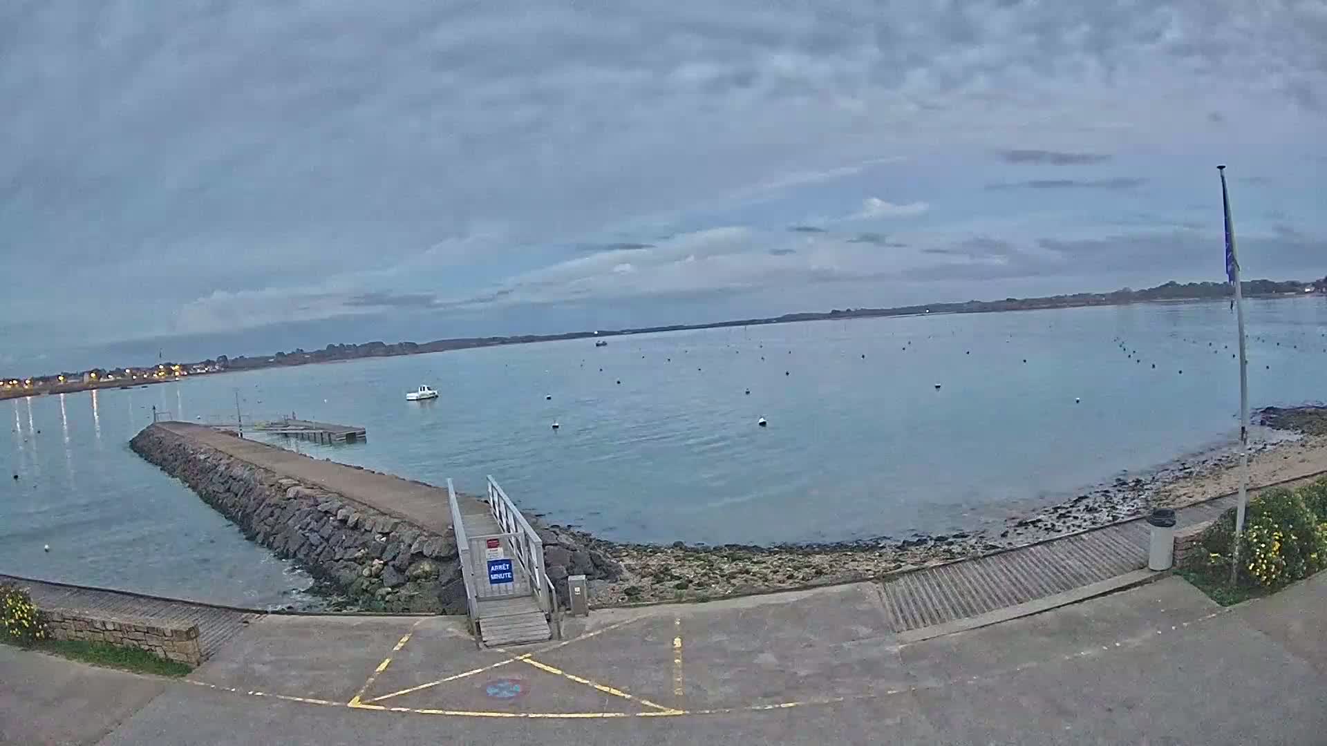 A calm body of water with a stone jetty and a small boat, under an overcast sky.